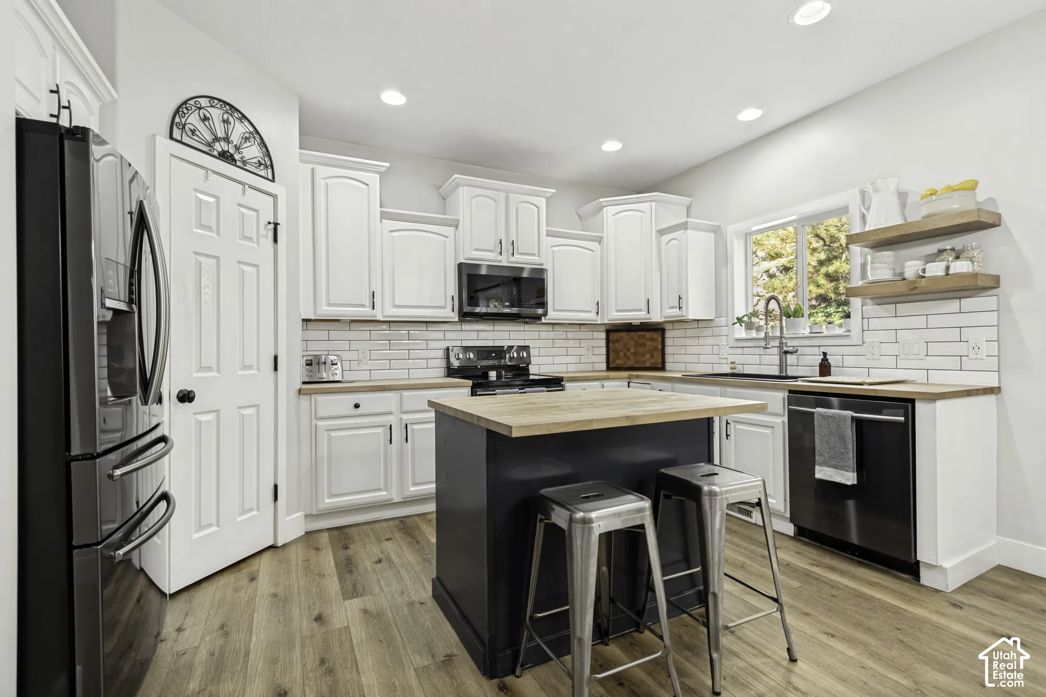 Kitchen featuring white shaker-style cabinetry, wood-finish countertops, a dark-toned center island, white subway tile backsplash, and recessed lighting