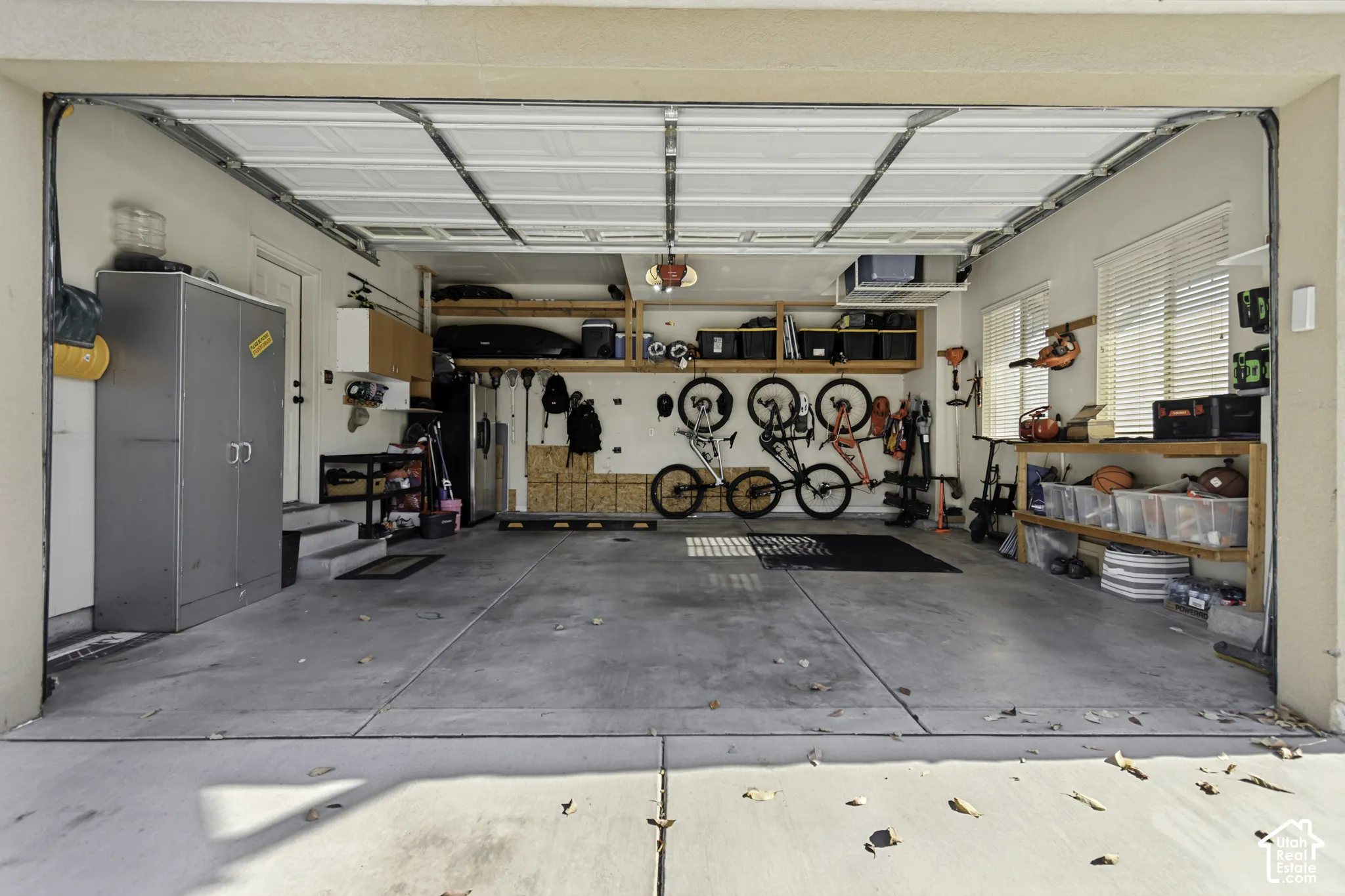 Attached two-car garage featuring concrete flooring, built-in wooden shelving, and dual windows with blinds