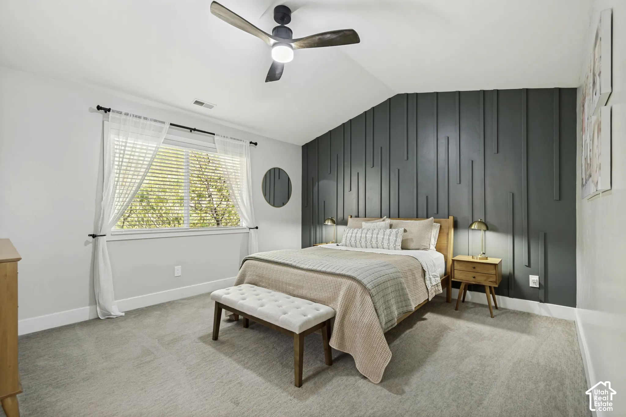 Vaulted ceiling featuring a dark green vertical slat accent wall, neutral carpeting, and a modern ceiling fan