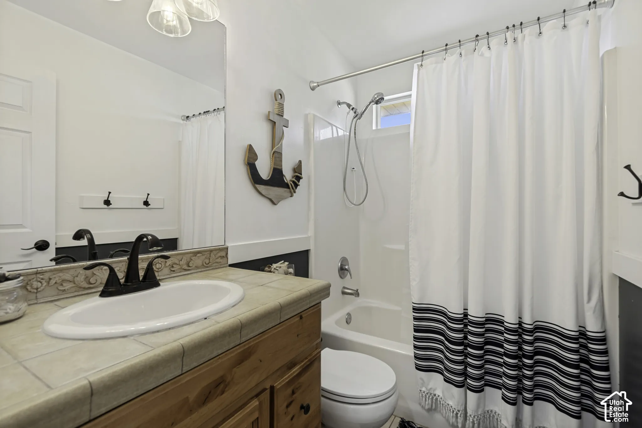 Bathroom featuring a tiled vanity countertop, oval drop-in sink with matte black hardware, wood-finish cabinetry, a large wall-mounted mirror, and a tub-shower combination with a detachable shower head