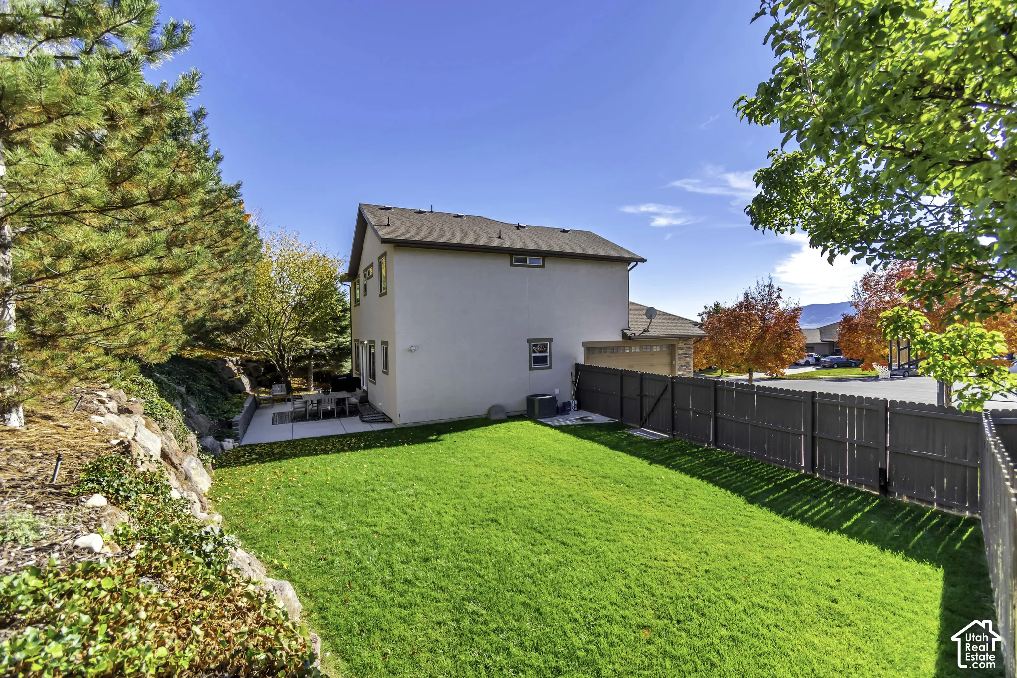 Private backyard featuring a manicured lawn, concrete patio, perimeter wood fencing, and terraced rock landscaping