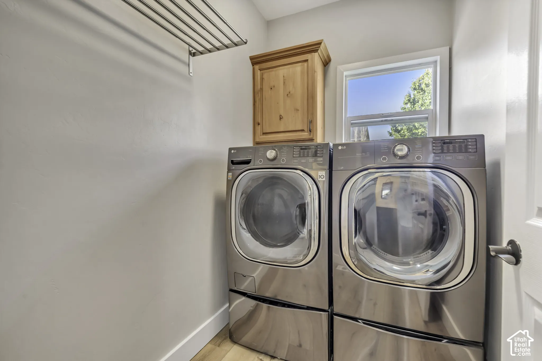 Utility space featuring a wall-mounted metal drying rack, natural wood-finish upper cabinetry, and a window for natural light