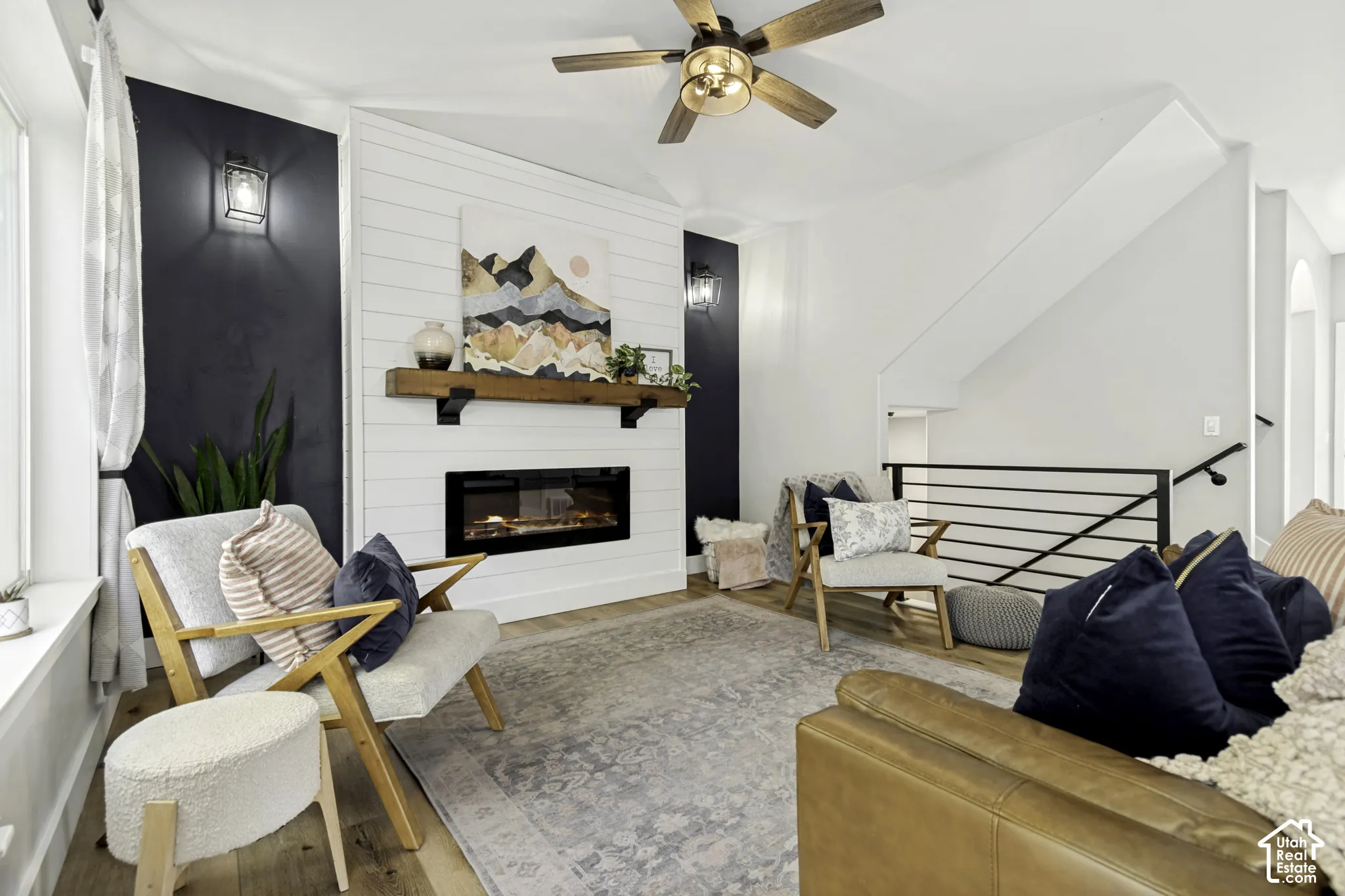 Fireplace featuring a custom shiplap surround, natural wood mantel, and built-in wall sconces, complemented by wood-finish flooring and a staircase with horizontal metal railing
