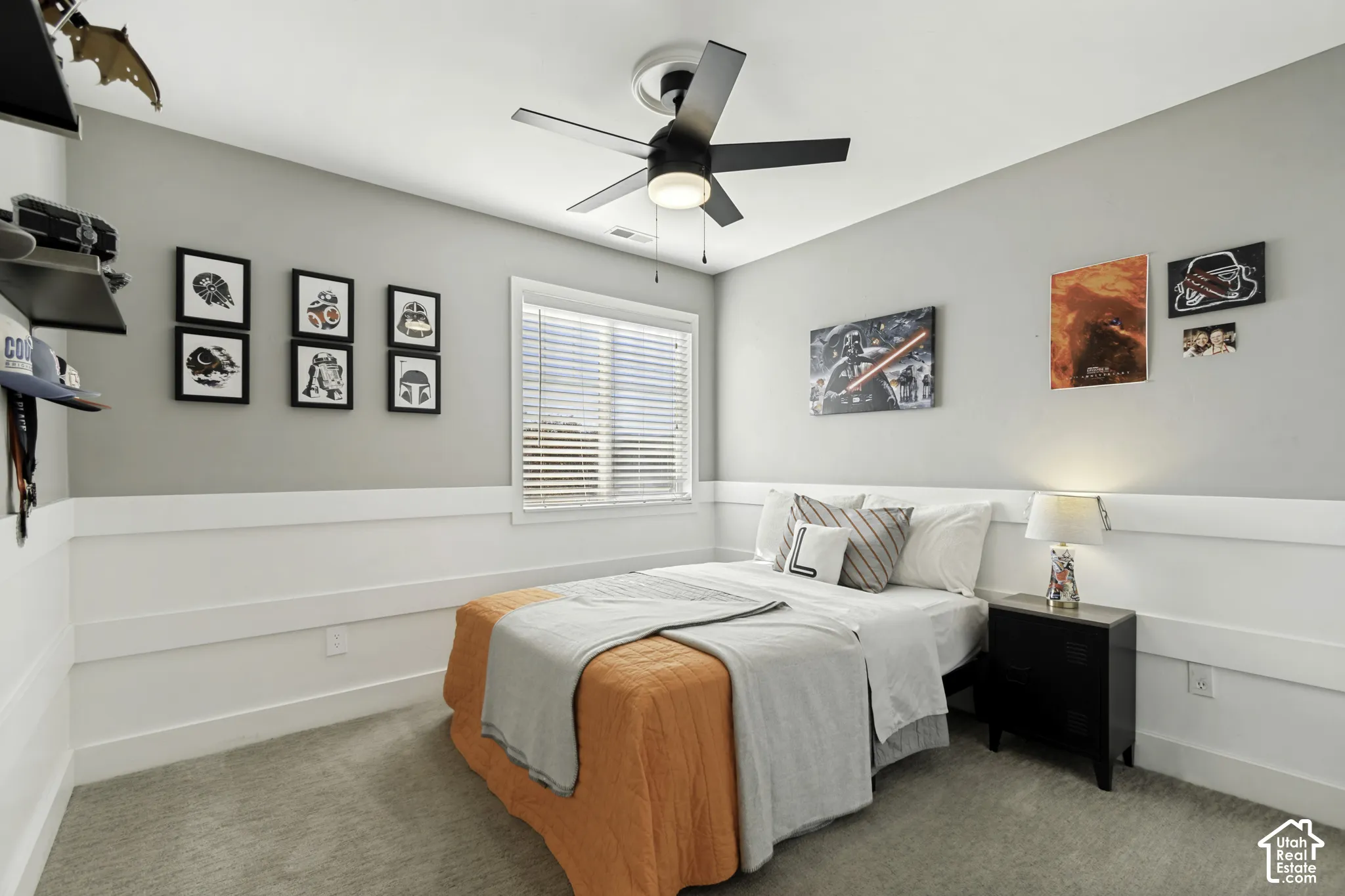 Bedroom featuring neutral wall-to-wall carpeting, horizontal board-and-batten wainscoting, a center-mounted ceiling fan with an integrated light fixture, and a single-hung window with blinds