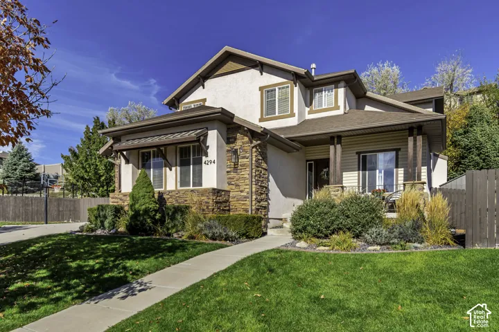 Two-story exterior featuring a mix of stucco and natural stone siding, multi-gabled roofline, metal awning detail, and covered front porch with timber posts