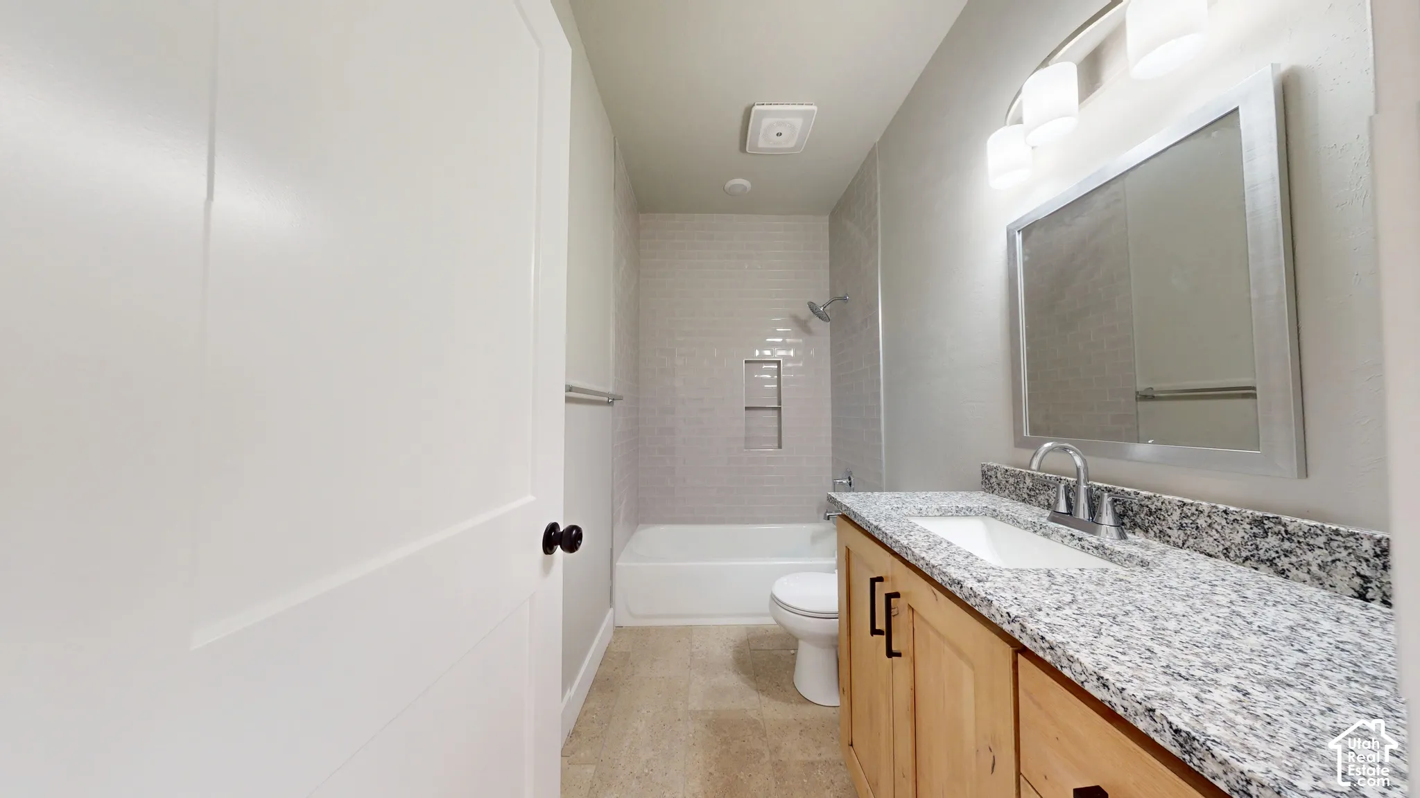 Bathroom featuring a stone-pattern countertop, wood cabinetry with matte black hardware, a recessed tile shower niche, and a three-light vanity fixture