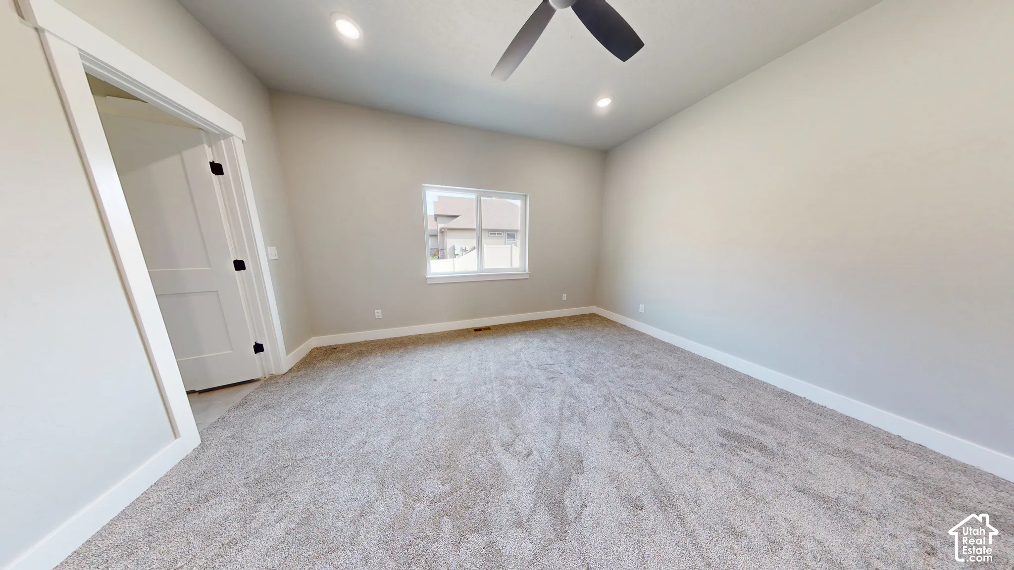 Neutral-toned interior space featuring carpeting, recessed lighting, a ceiling fan, and a single-panel door with matte black hardware