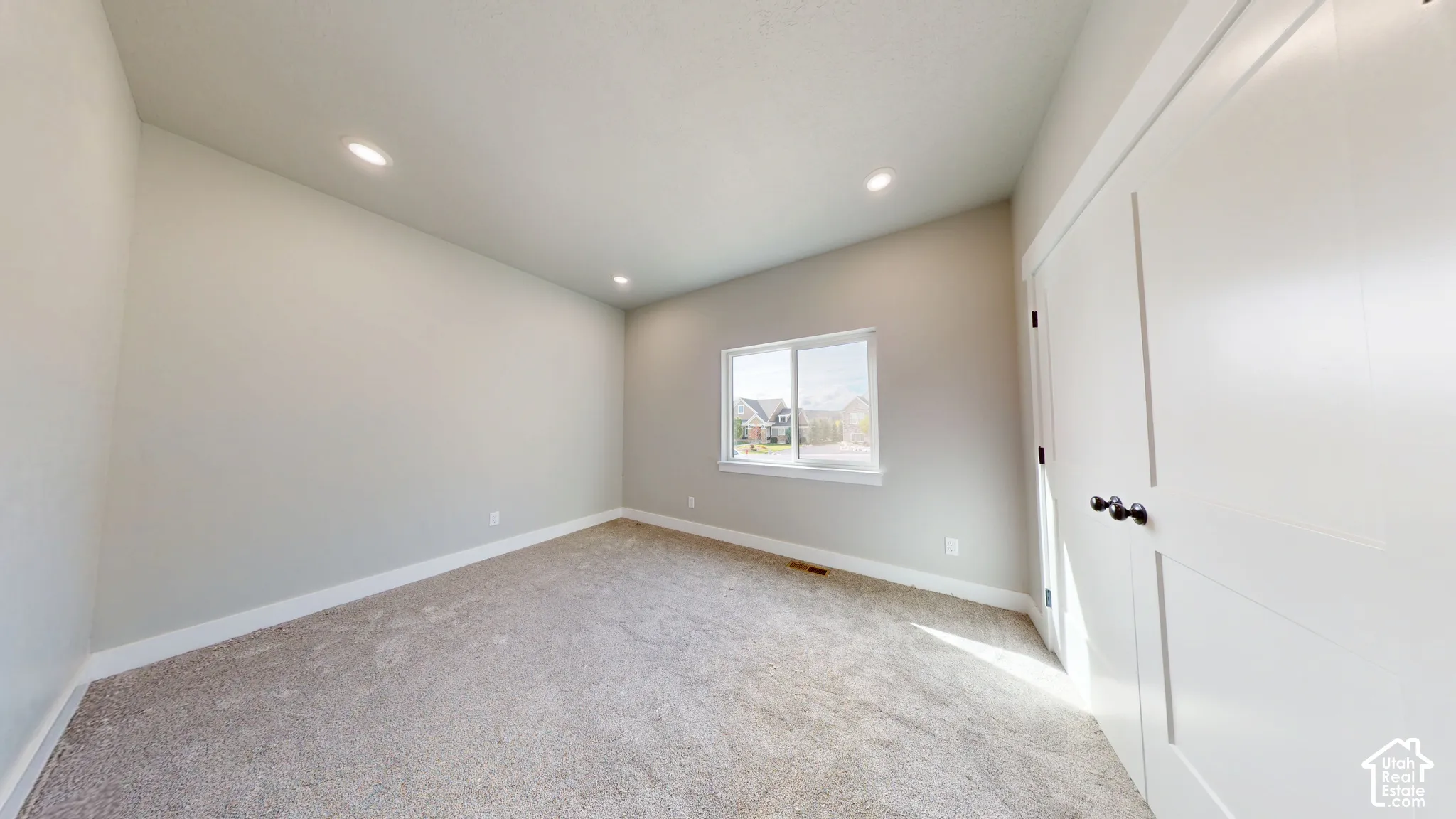 Neutral-toned interior featuring wall-to-wall carpeting, recessed lighting, a sliding-sash window, and double-panel closet doors with matte black hardware