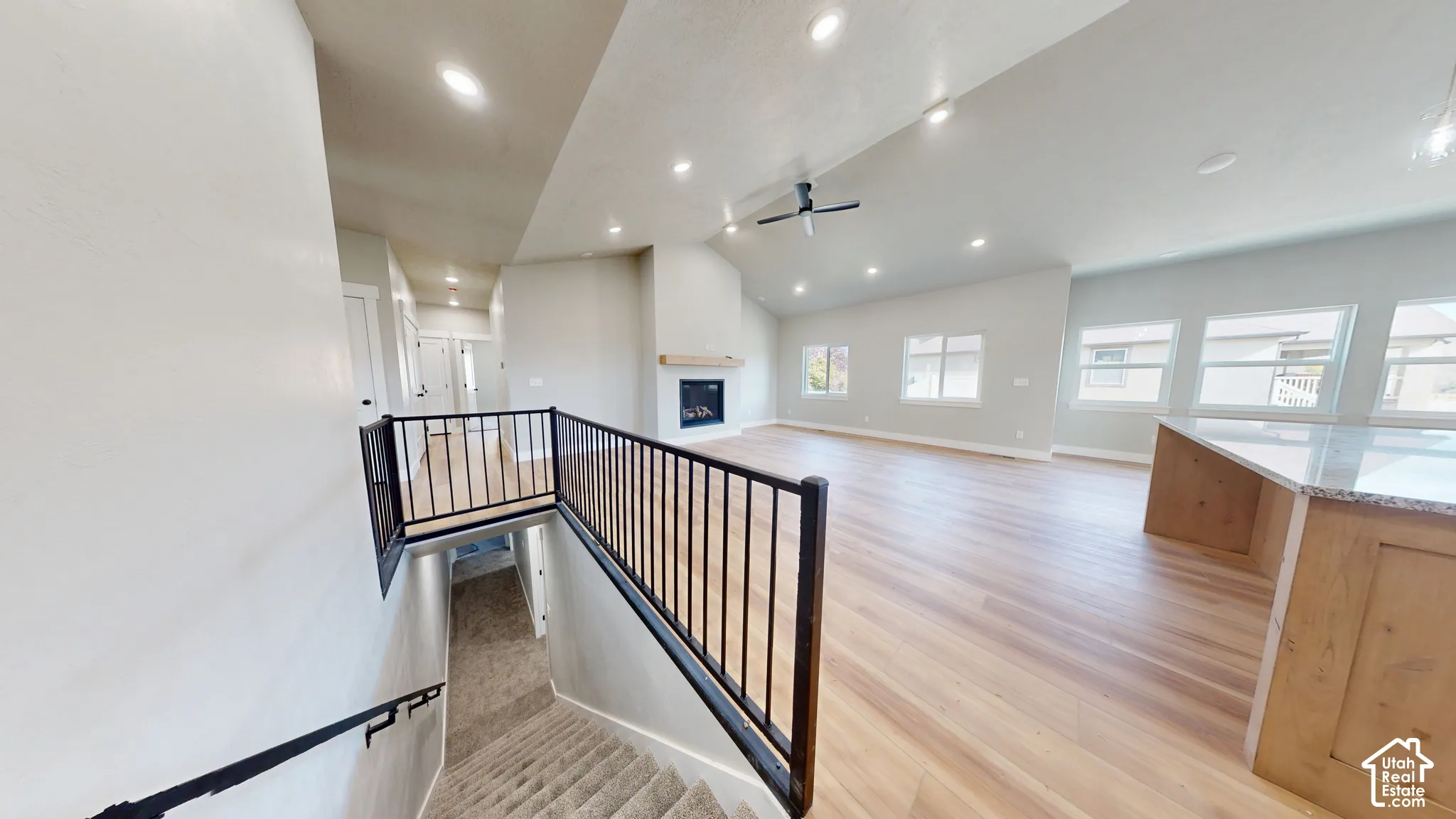 Open-concept interior featuring vaulted ceilings, recessed lighting, wood-finish flooring, a fireplace with a wood mantel, and a metal stair railing