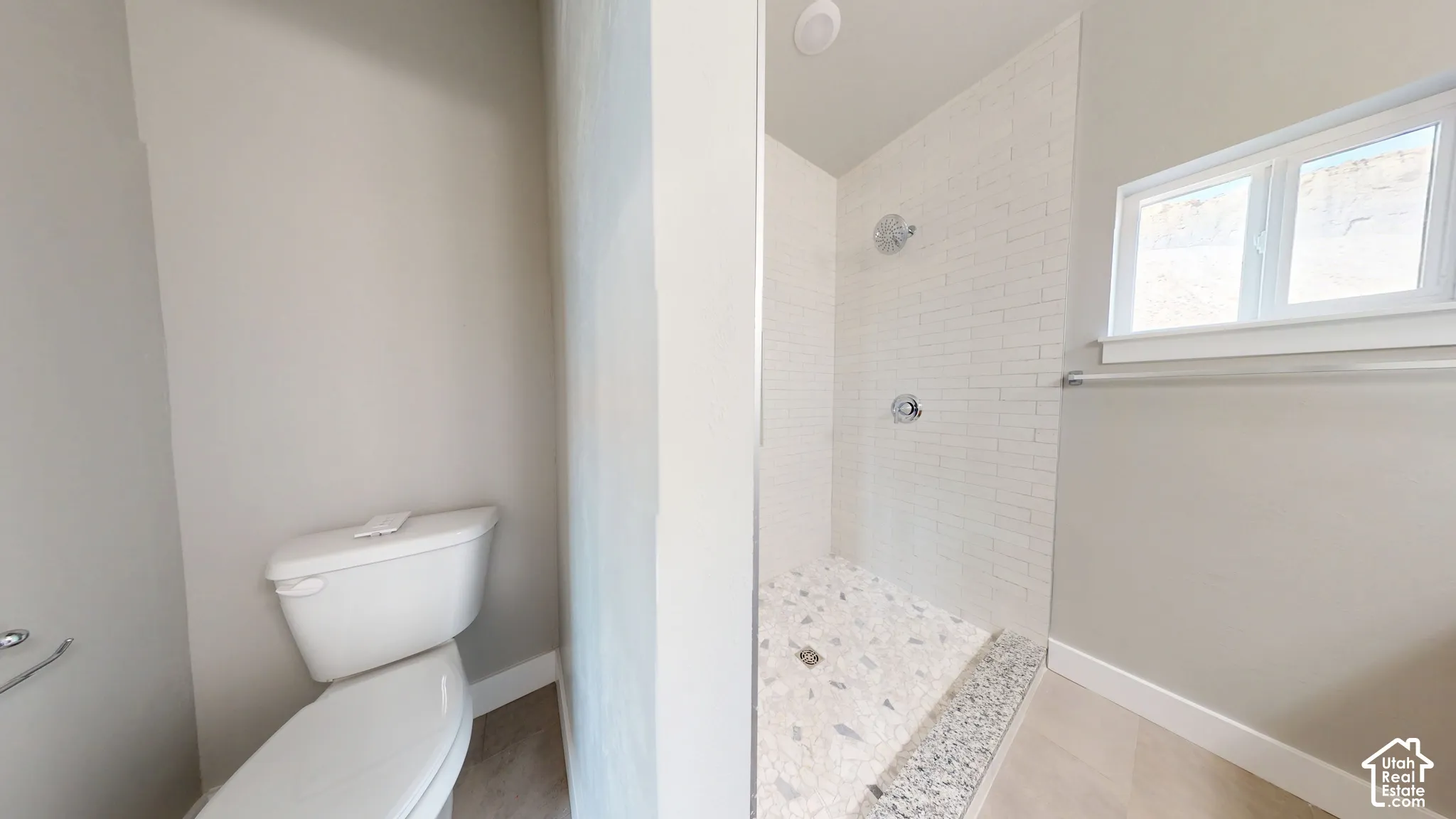 Shower featuring white subway tile walls, a pebble-finish floor, a horizontal window, and polished chrome fixtures, paired with a white porcelain toilet