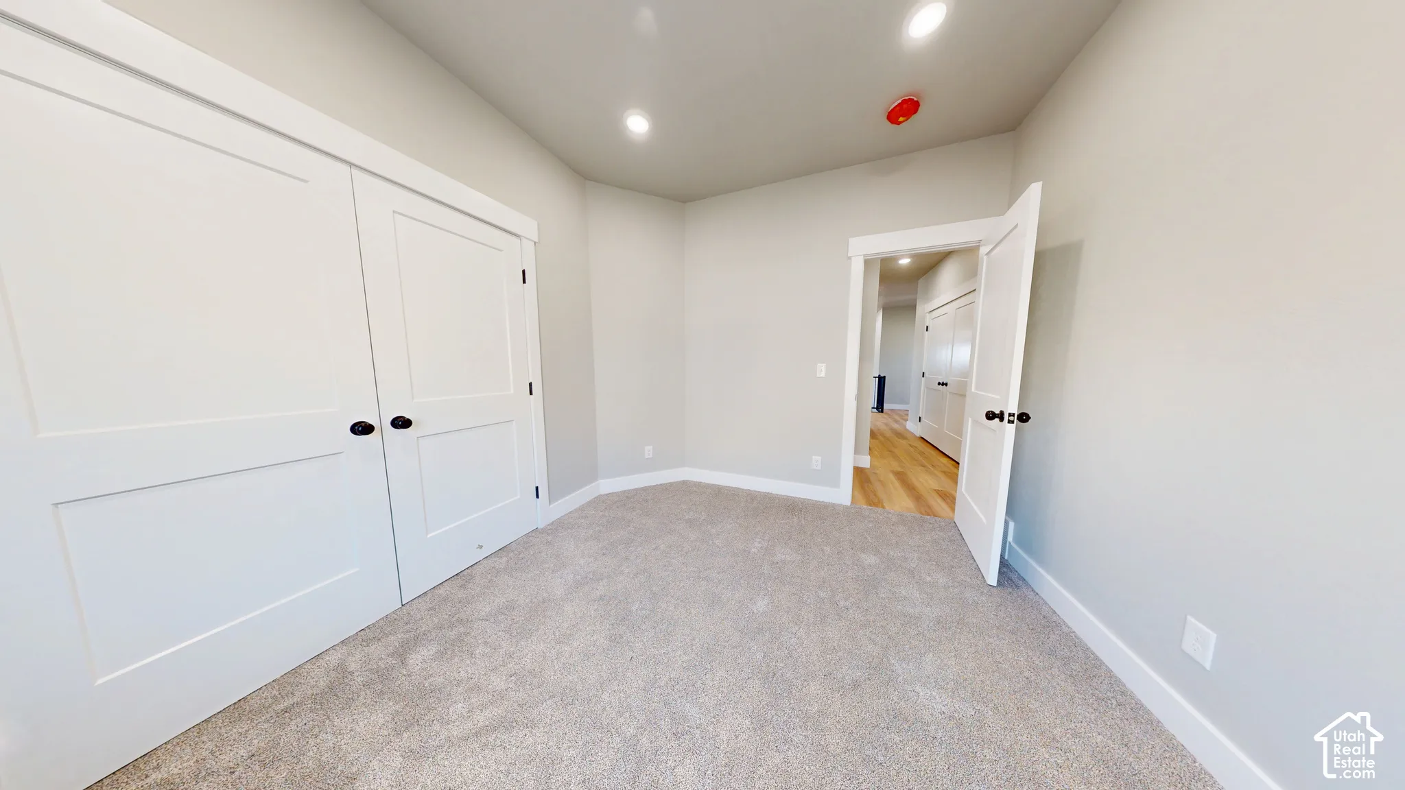Interior space featuring neutral wall tones, plush wall-to-wall carpeting, recessed ceiling lighting, and double-panel closet doors with matte black hardware