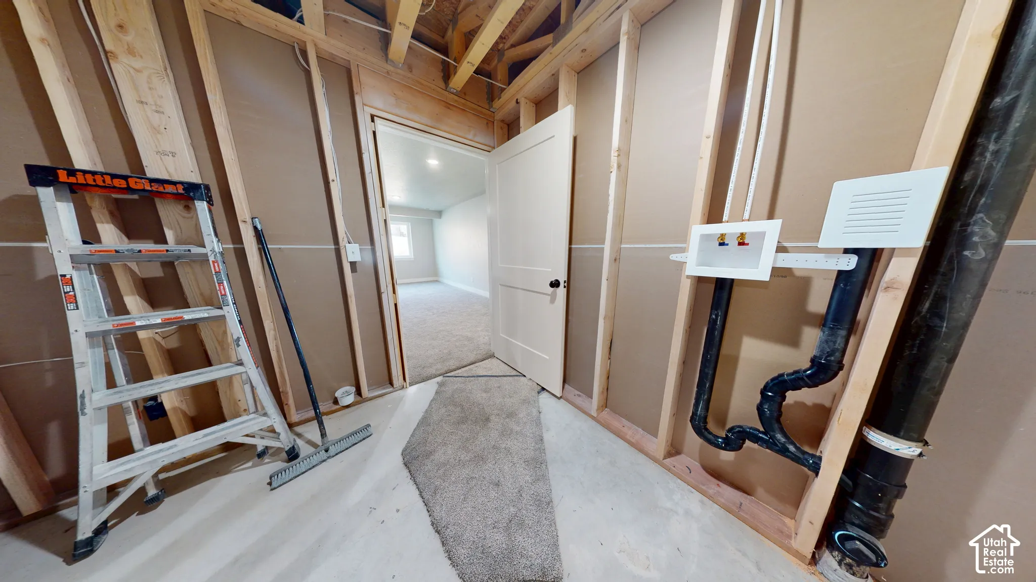 Utility space featuring exposed wood framing, installed washer and dryer hookups, and a white interior door