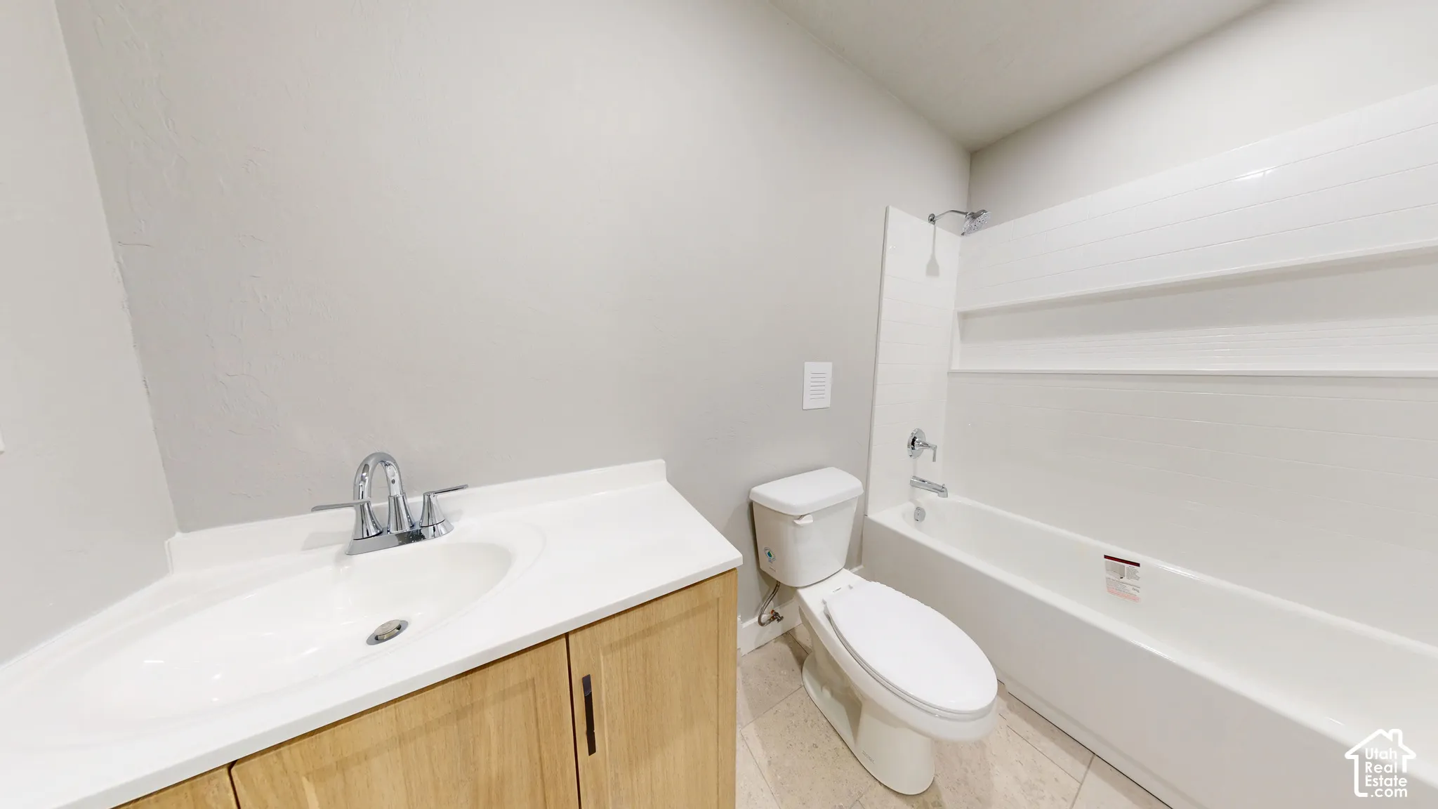 Bathroom featuring a wood-finish vanity with a stone-top integrated sink, chrome dual-handle faucet, white toilet, and a tub-shower combination with built-in shelving and a chrome fixture