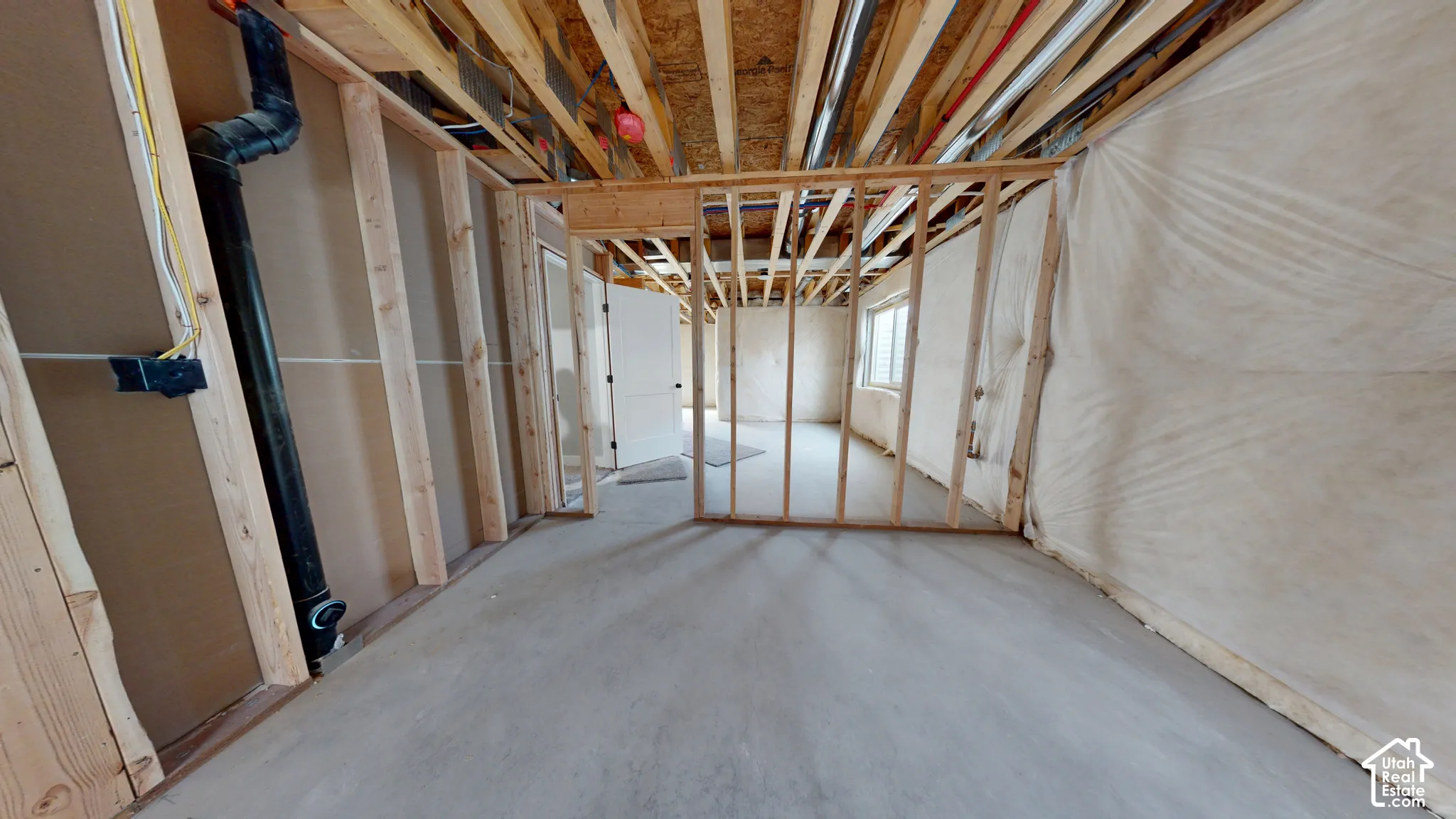 Unfinished lower level featuring exposed wood framing, concrete flooring, and an installed door