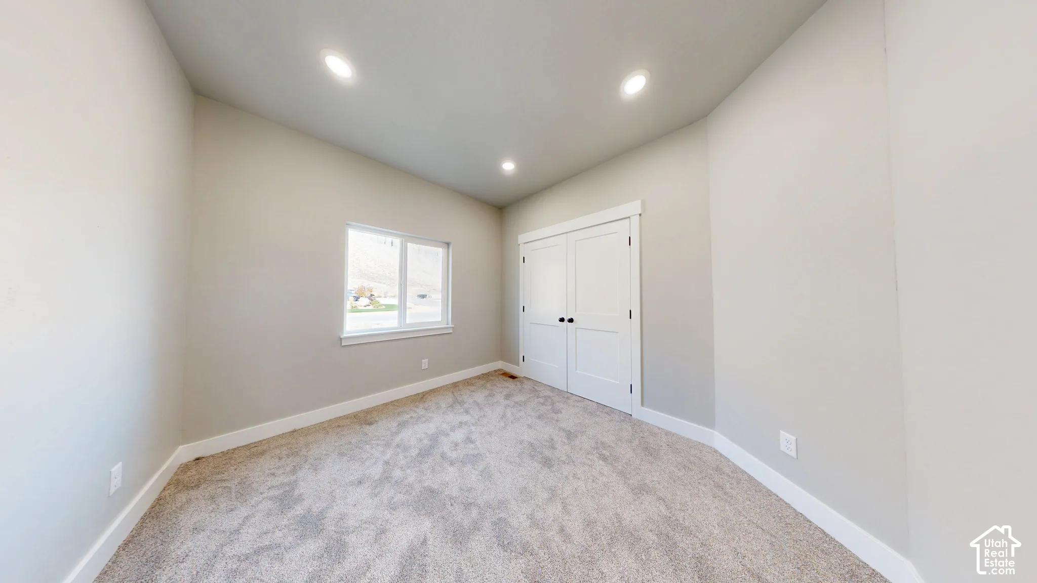 Neutral-toned room featuring recessed ceiling lighting, wall-to-wall carpeting, a single-pane window, and double doors with dark hardware