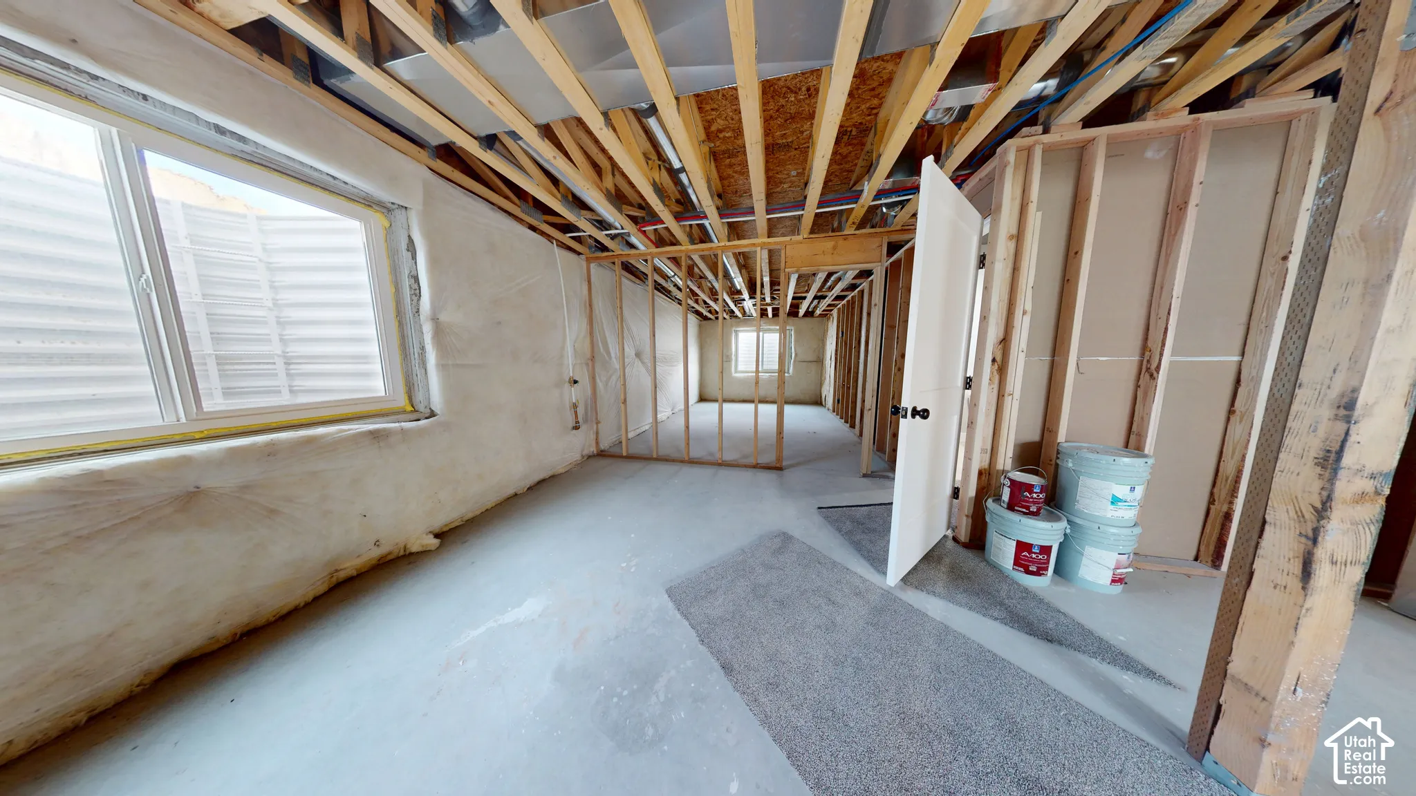 Unfinished interior space featuring exposed wood framing, concrete flooring, insulated walls, and two large egress windows