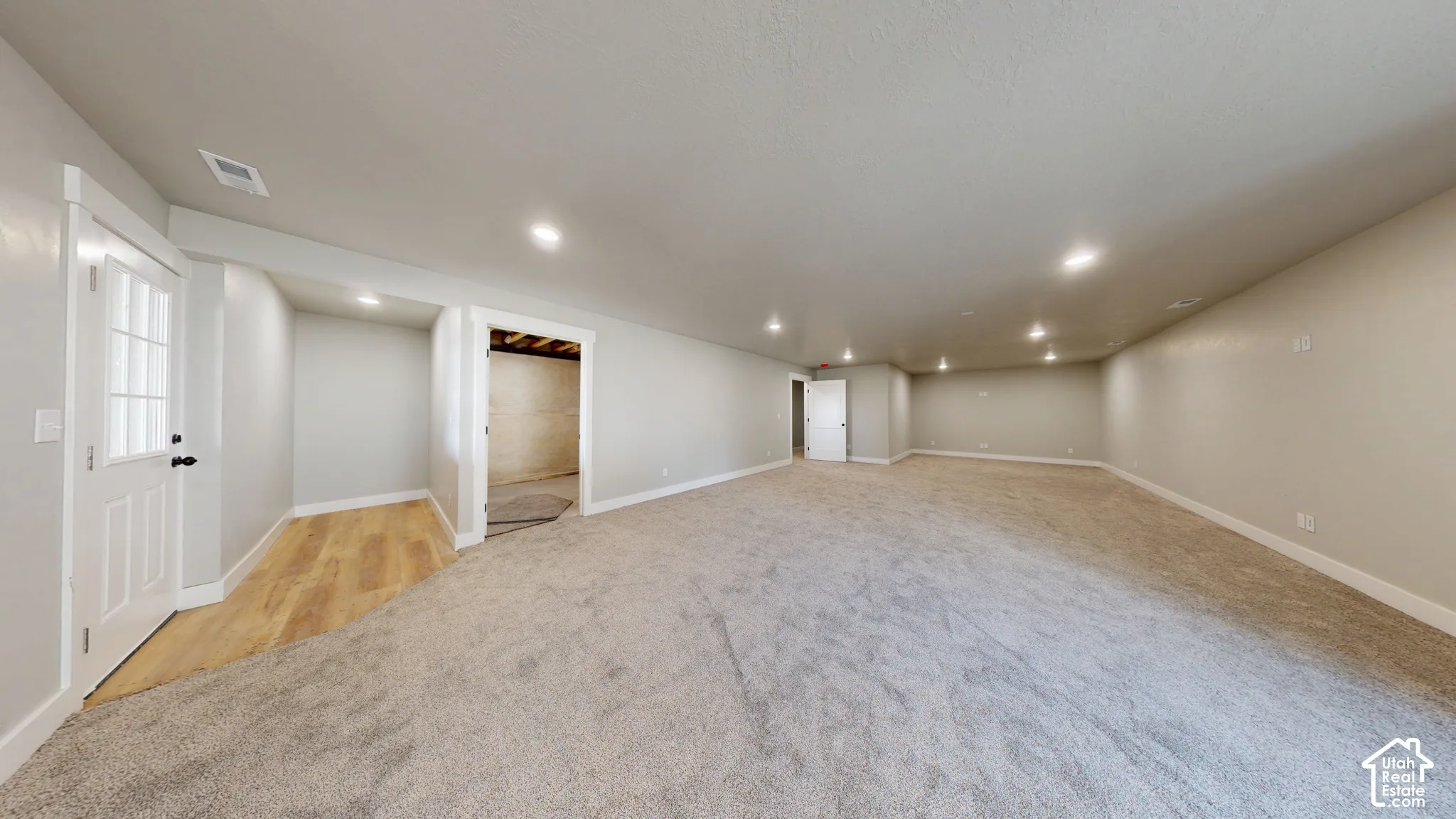 Open-concept room featuring neutral wall paint, wall-to-wall carpeting, recessed ceiling lighting, and a multi-lite exterior door with wood-finish flooring at the threshold