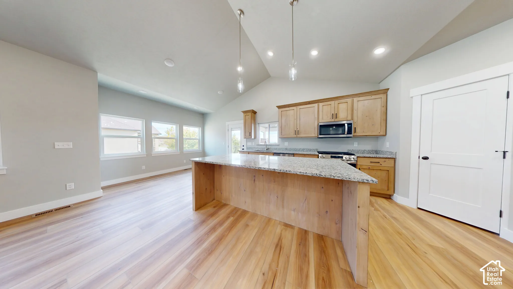 Kitchen featuring wood-finish cabinetry, stone-surface countertops, central island, vaulted ceilings, and wood-finish flooring
