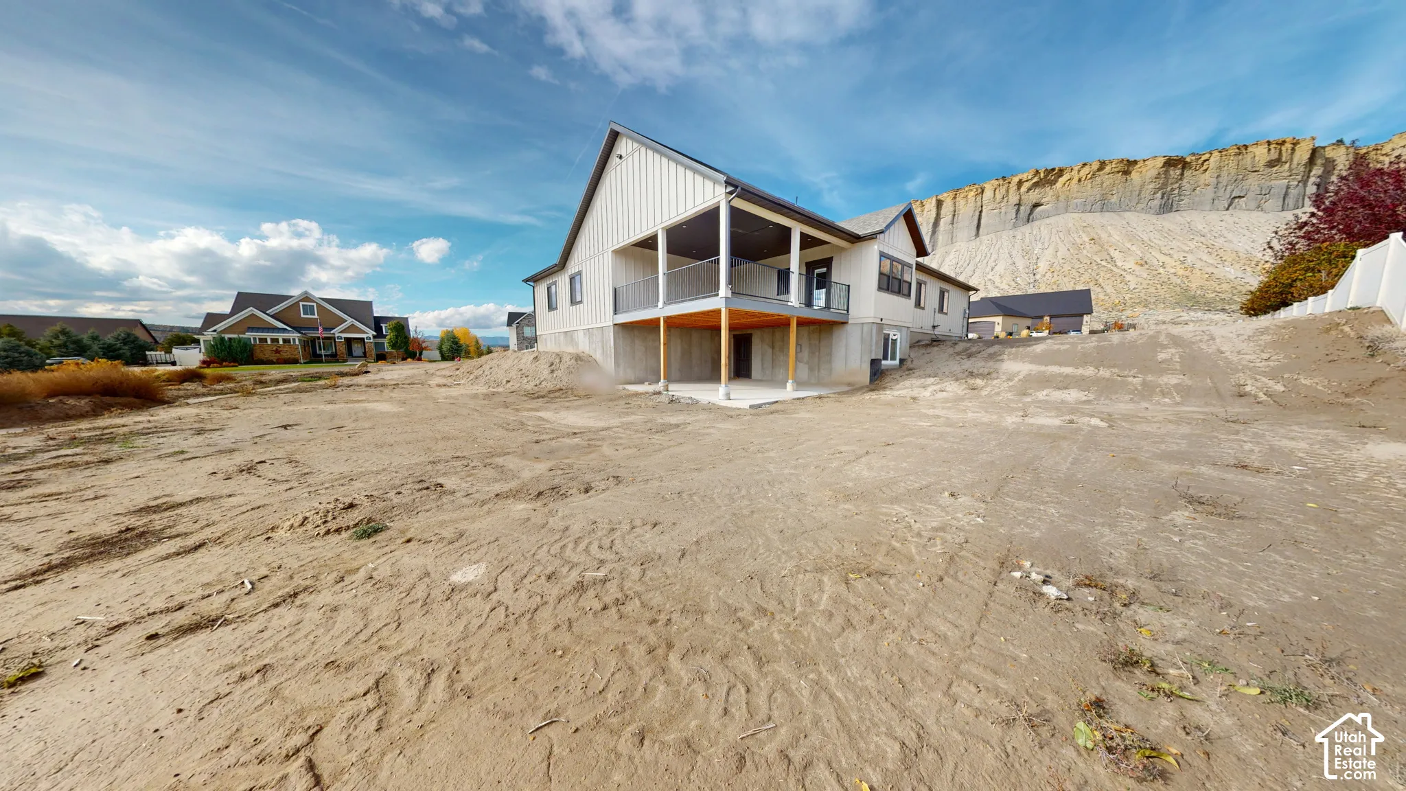 Exterior featuring vertical siding, a covered balcony with metal railing, a concrete foundation, and a concrete patio set against a mountain backdrop