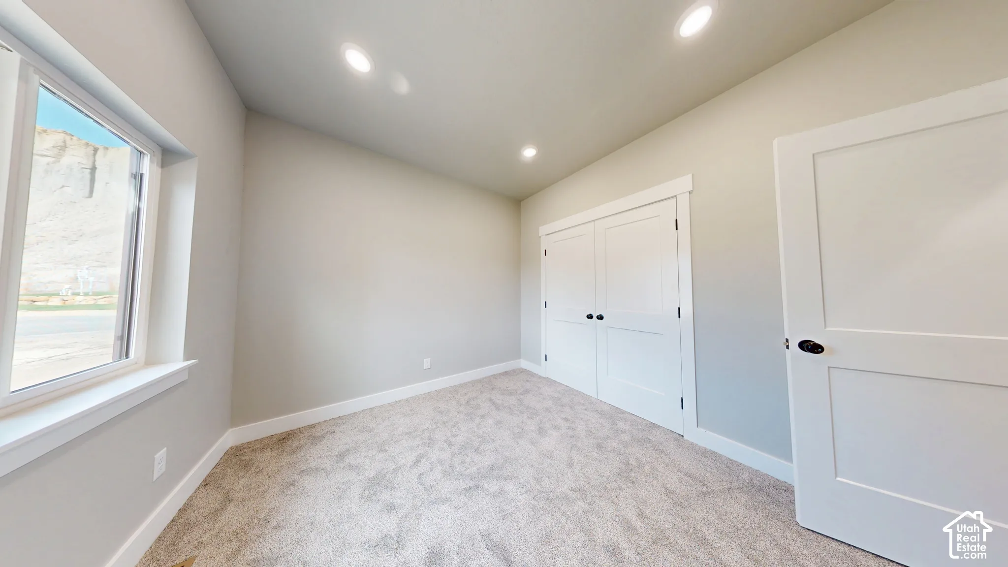 Neutral-toned interior featuring recessed lighting, wall-to-wall carpeting, dual-panel closet doors with matte black hardware, and a single-hung window with a sill