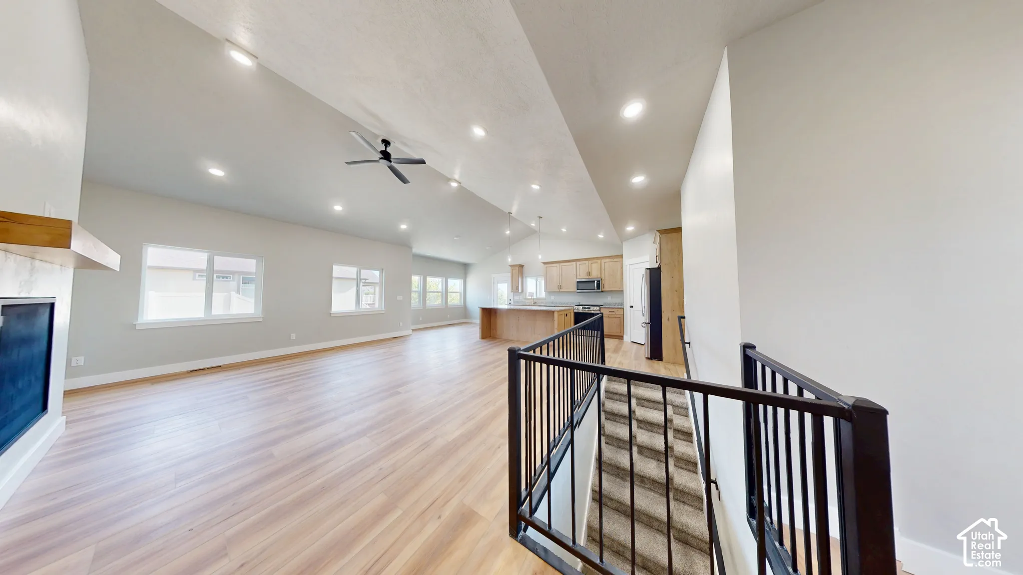 Vaulted ceilings with recessed lighting, wood-finish flooring, built-in fireplace with wooden mantel, and staircase featuring a black metal railing