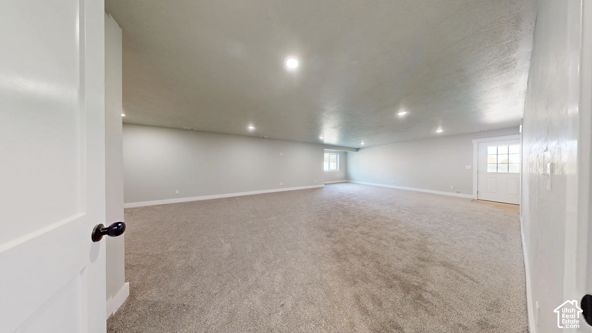 Expansive open interior space featuring recessed ceiling lighting, wall-to-wall carpeting, neutral wall finishes, and an exterior door with glass panes