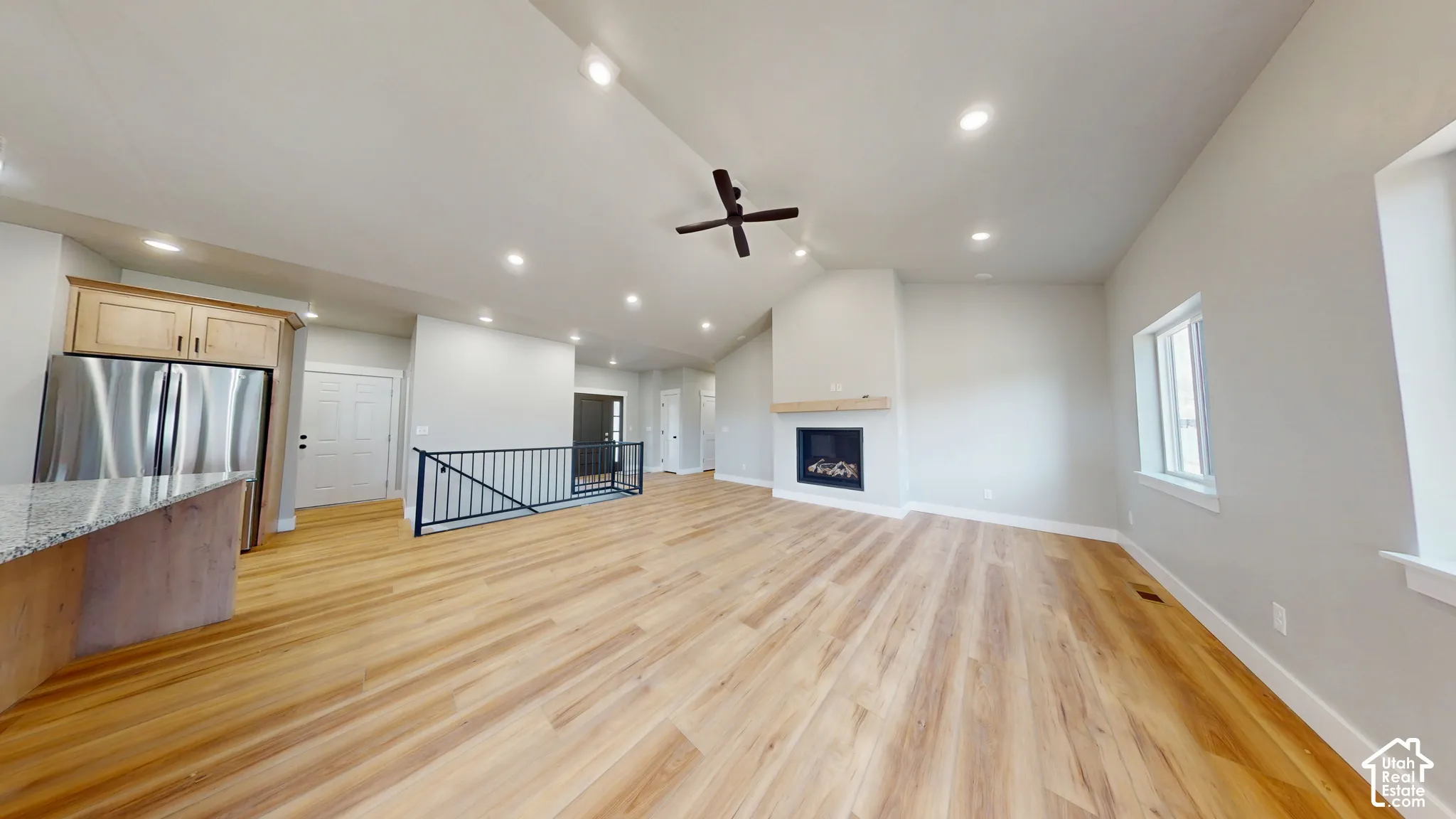 Open floor plan featuring wood-finish flooring, vaulted ceilings with recessed lighting, a fireplace with a wood mantel, and a kitchen island with stone-style countertops