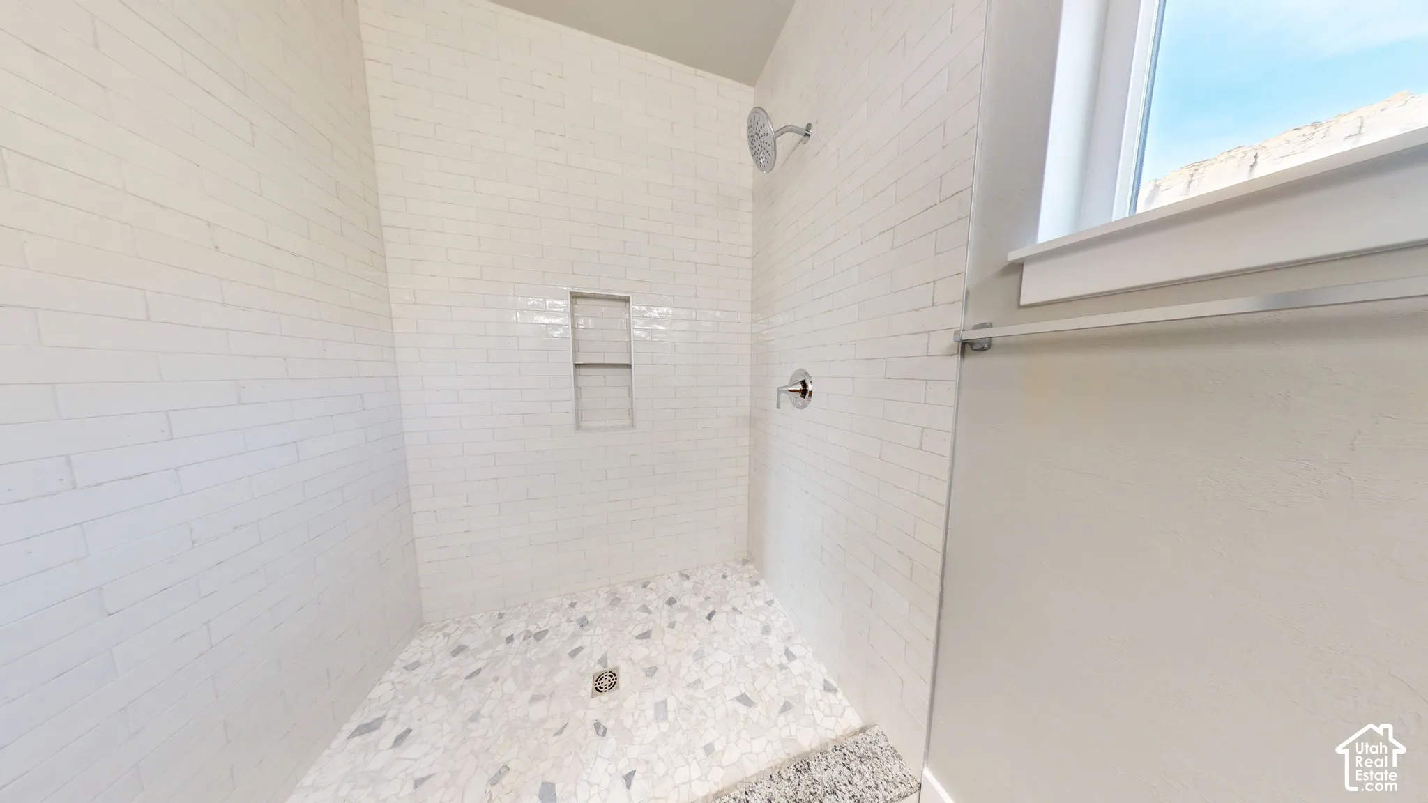Walk-in shower featuring white elongated wall tiles, mosaic stone floor tiling, a recessed wall niche, and a wall-mounted shower head