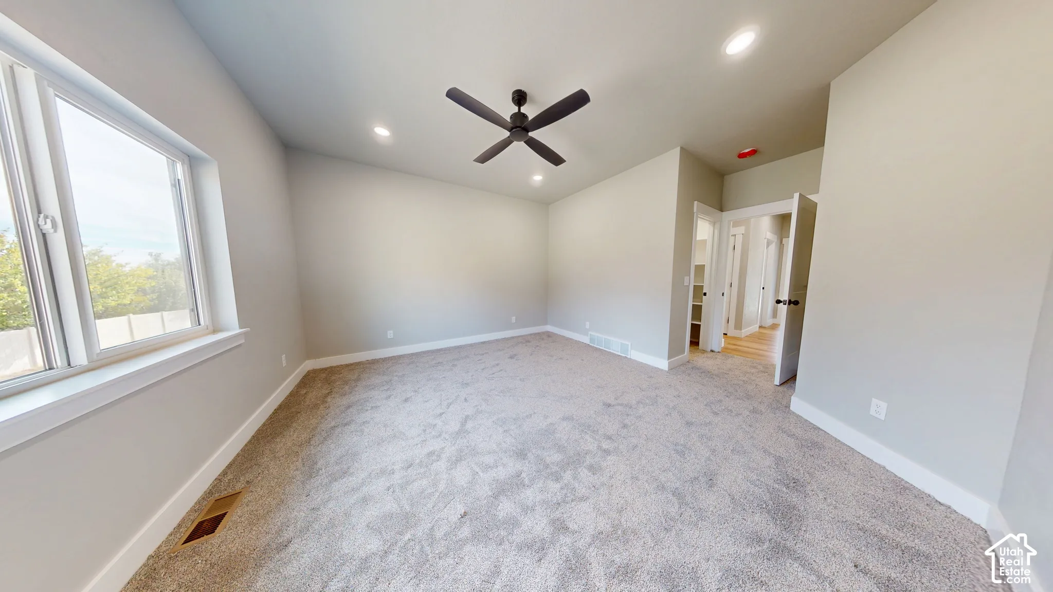 Neutral-toned interior featuring wall-to-wall carpeting, recessed ceiling lighting, a dark-finish matte ceiling fan, and large windows with casing