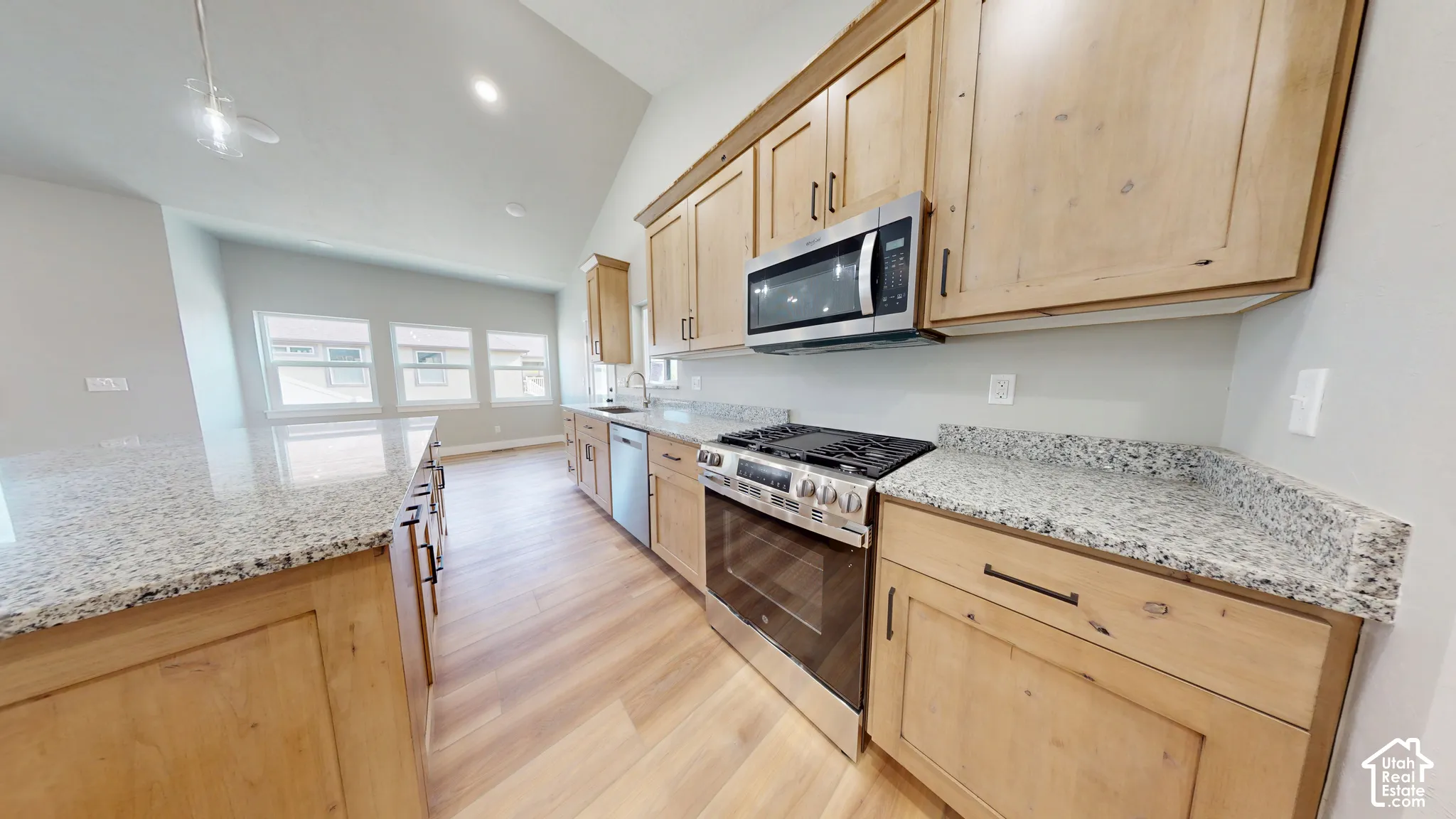 Kitchen featuring natural wood cabinetry, stone-surface countertops, stainless steel appliances, wood-finish flooring, and a vaulted ceiling