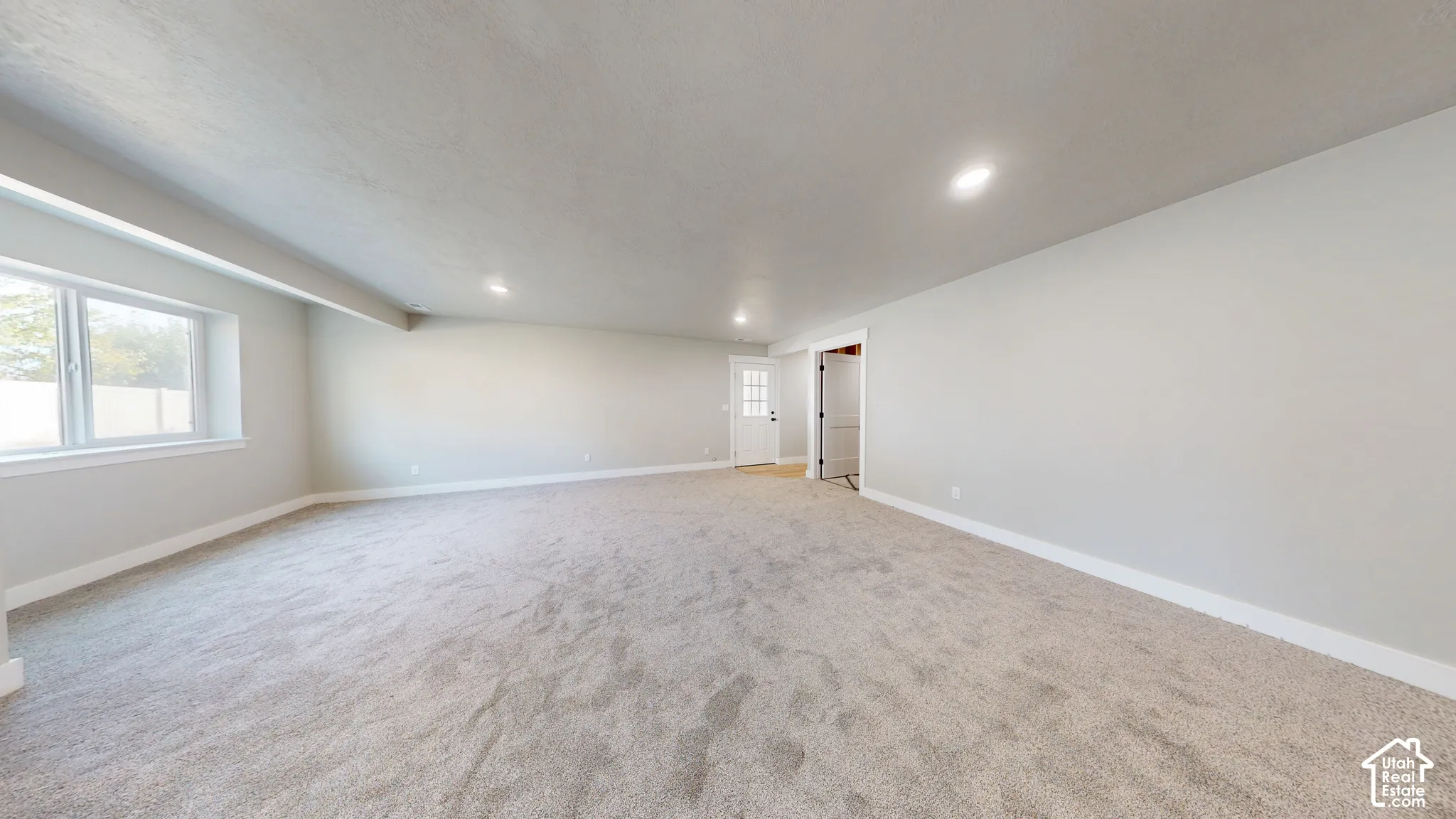 Neutral-toned interior space featuring light-colored wall-to-wall carpeting, recessed ceiling lighting, a large window, and a multi-panel exterior entry door