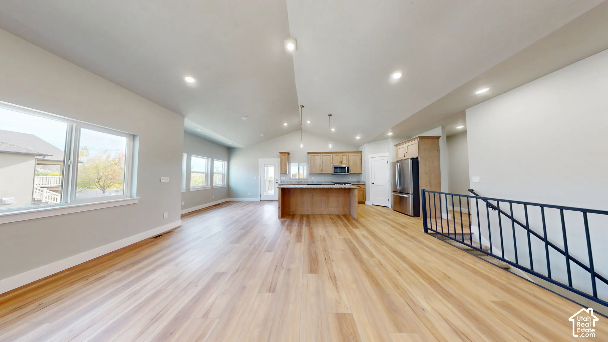 Open-concept area featuring vaulted ceilings, wood-finish flooring, a kitchen island, recessed lighting, and a metal stair railing