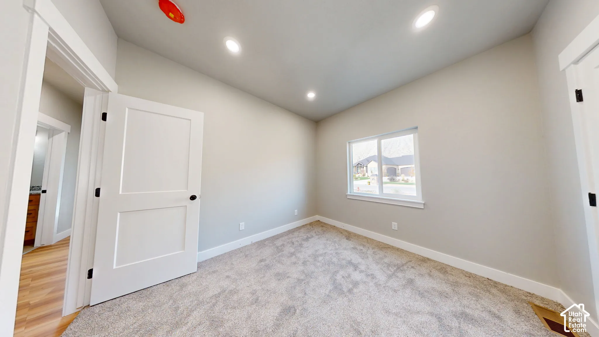 Neutral-toned interior featuring recessed lighting, plush wall-to-wall carpeting, and a single-hung window with white casing