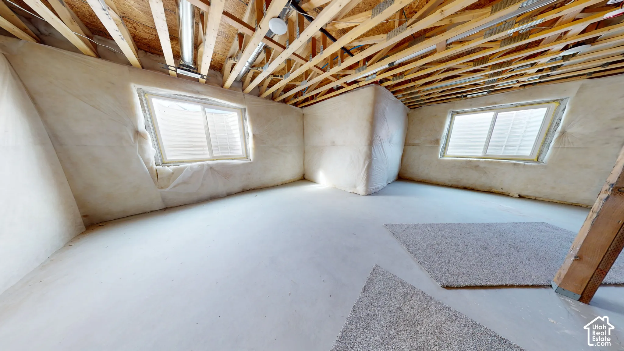 Unfinished interior space featuring exposed wood-truss ceiling, concrete flooring, dual sliding egress windows, and insulated wall paneling