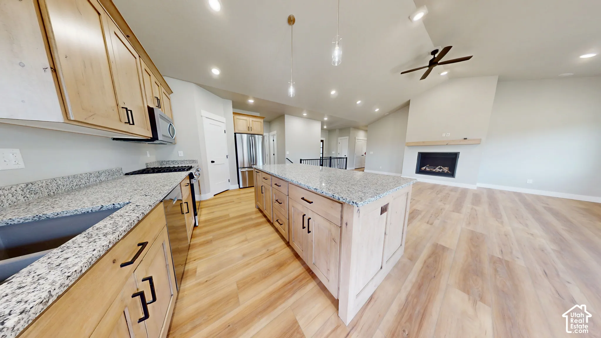 Kitchen featuring light-finish cabinetry, stone countertops, central island, wood-finish flooring, and a fireplace with a wood mantel