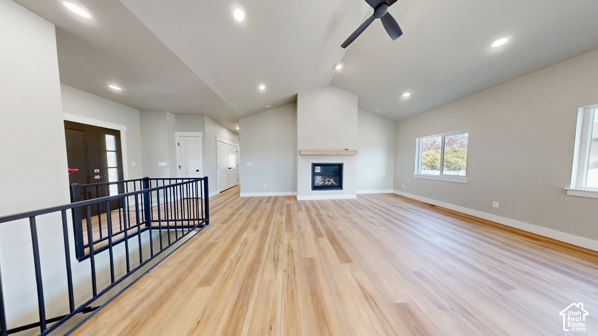 Vaulted ceilings, wood-finish flooring, recessed lighting, fireplace with a wood mantel, and a matte black metal railing