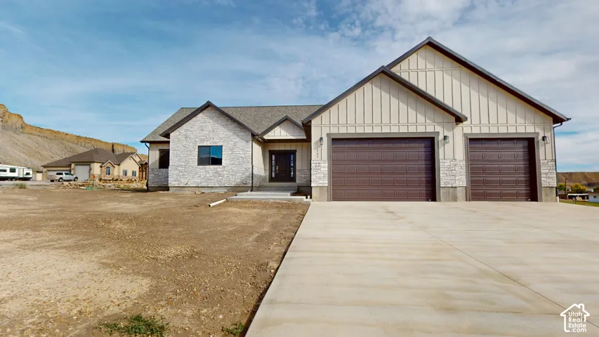 Single-story exterior featuring board-and-batten siding, stone masonry accents, a three-car garage, and a concrete driveway