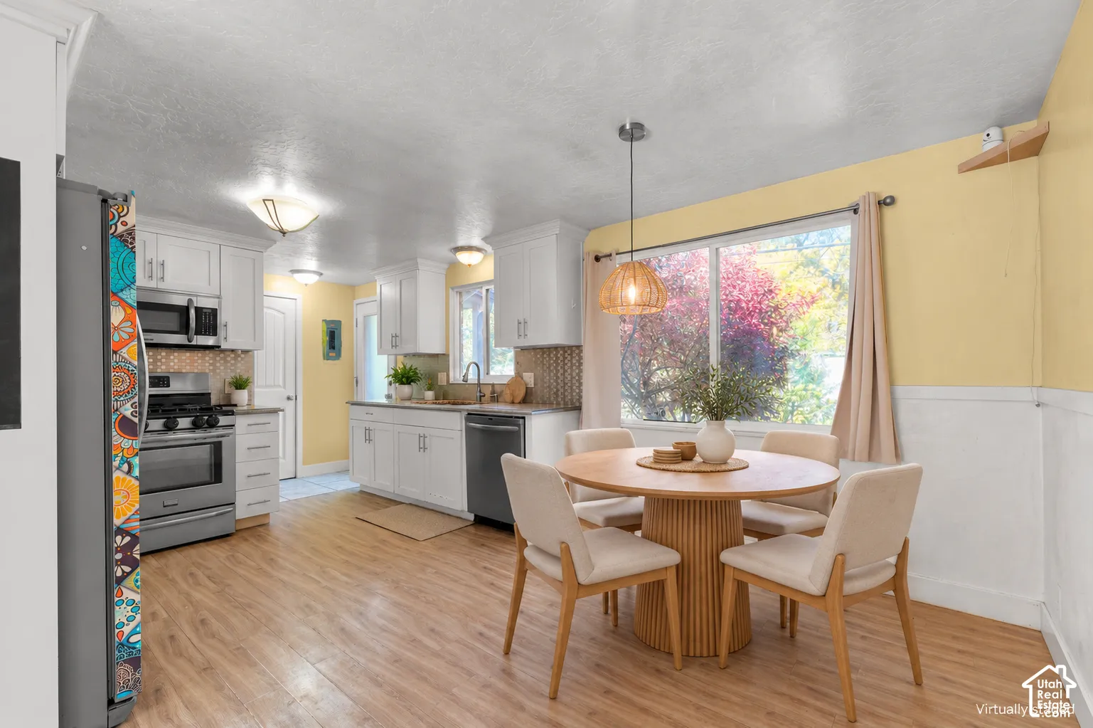 Kitchen featuring white cabinetry, wood-finish flooring, stainless steel appliances, patterned tile backsplash, and a pendant light fixture