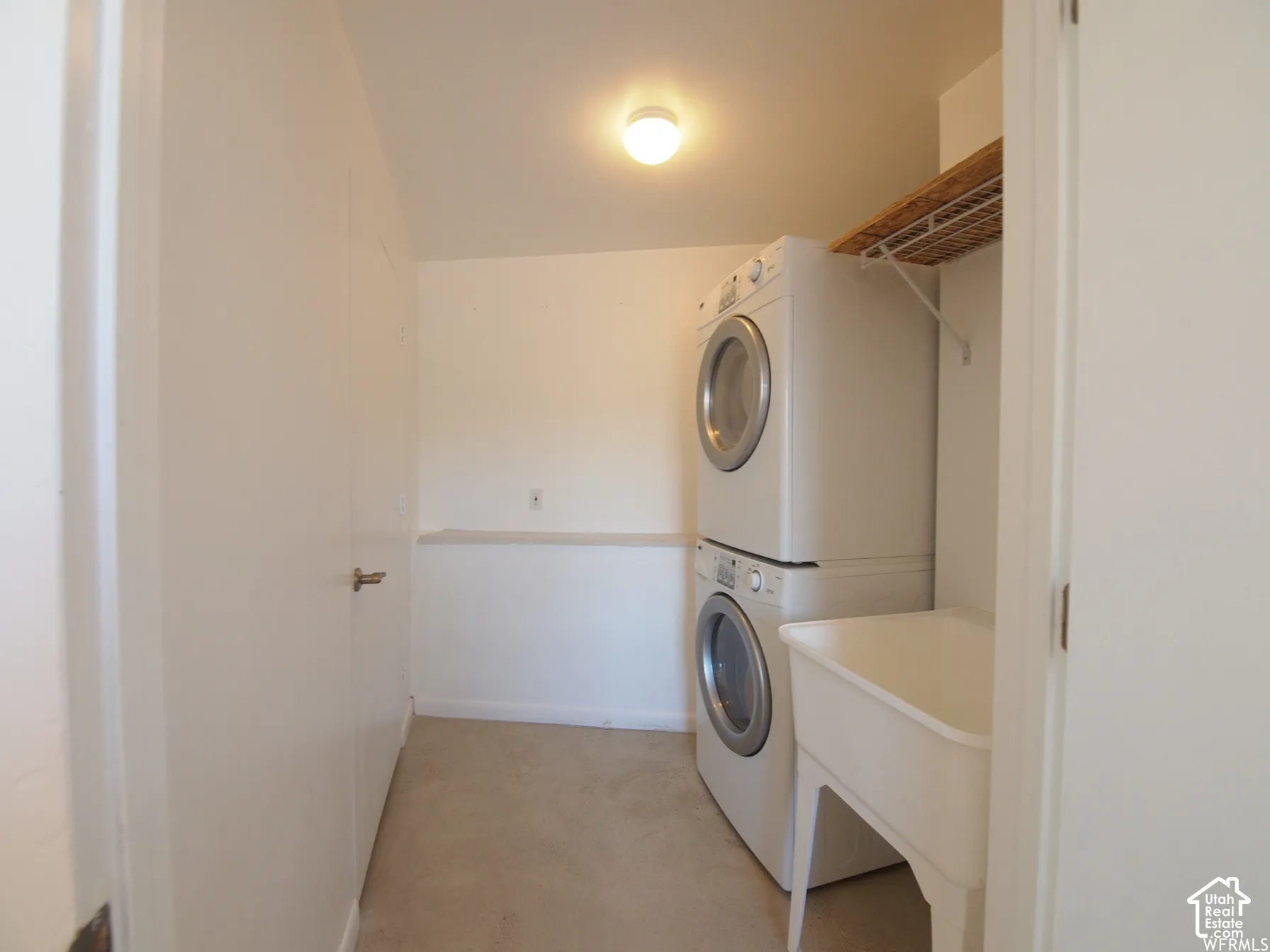 Laundry area featuring a stackable washer and dryer, utility basin, wall-mounted wire shelving, and flush-mount ceiling lighting