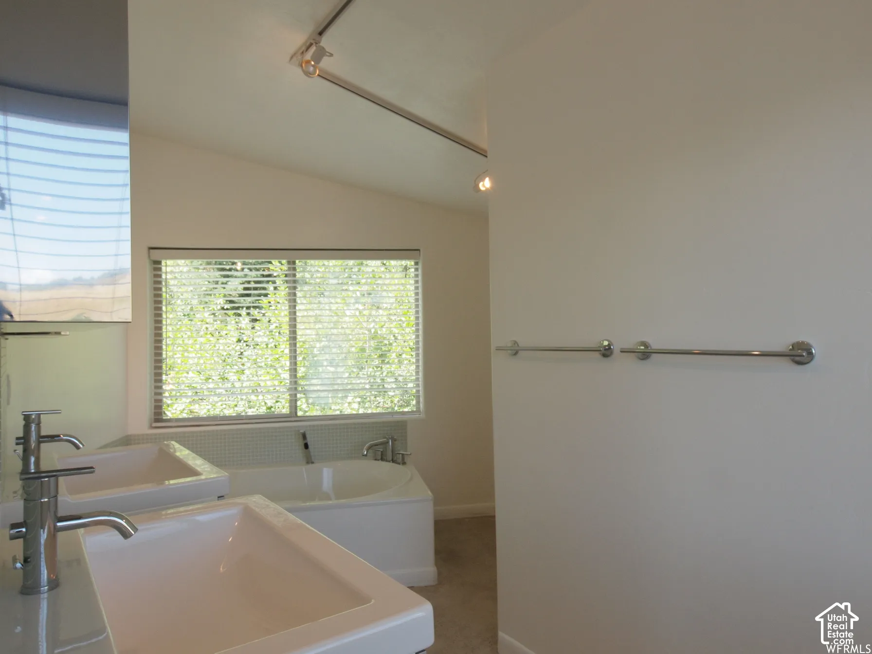 Dual vanity featuring rectangular vessel sinks and metal faucets, soaking tub with tile surround, and overhead track lighting