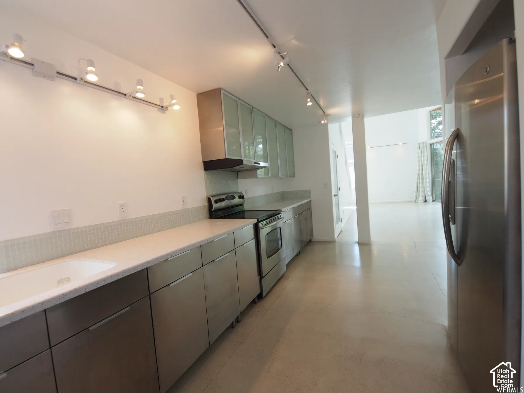 Kitchen featuring stainless steel cabinetry, matte-finish countertops, stainless steel appliances, frosted-glass upper cabinets, and adjustable track lighting