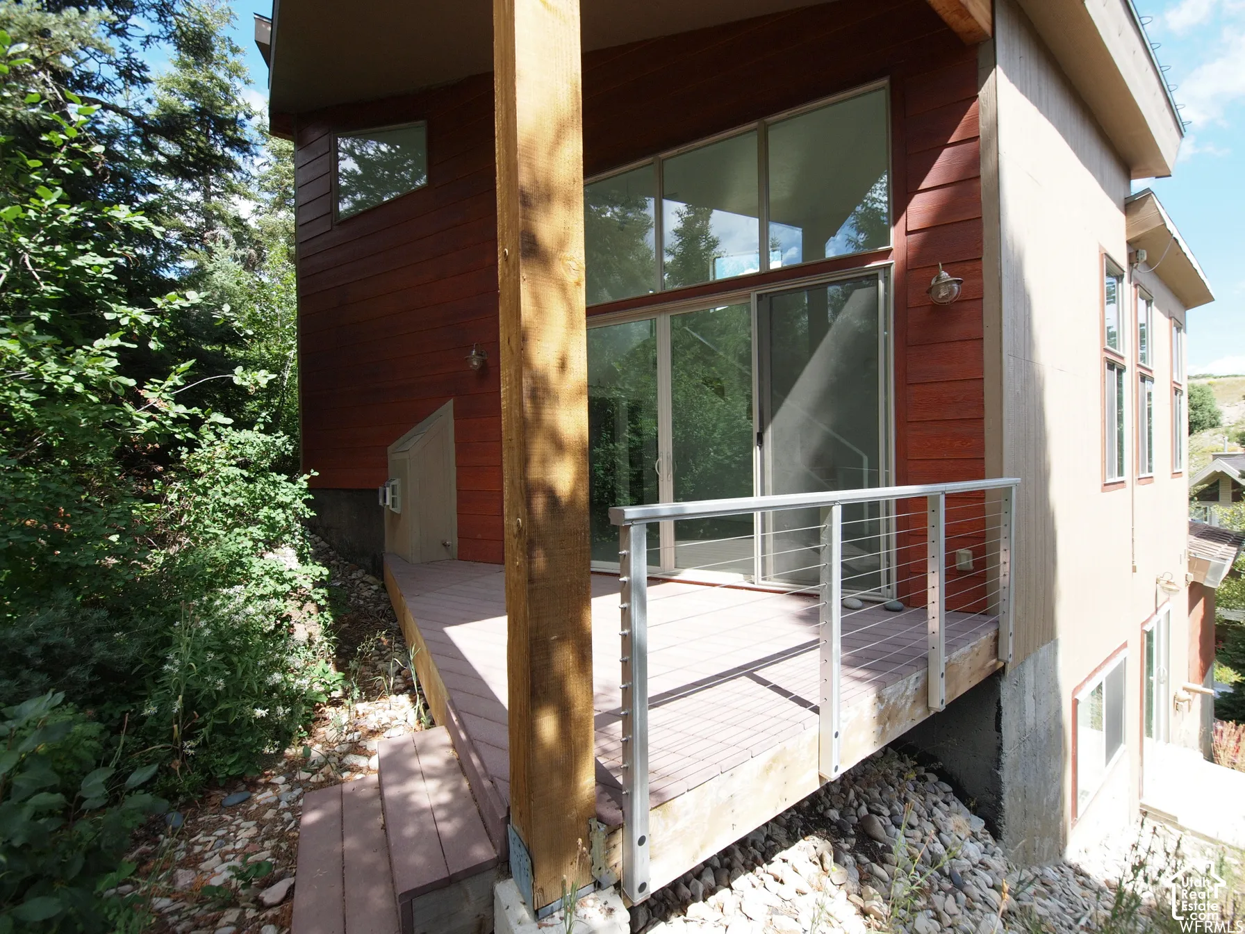 Exterior deck with cable railing, wood siding, large floor-to-ceiling glass sliding doors, and expansive transom windows