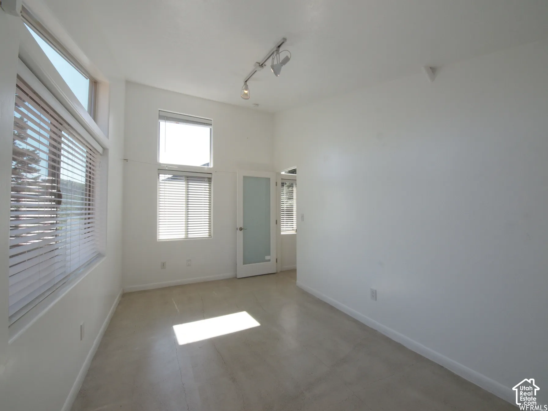 High ceilings featuring adjustable track lighting, large multi-pane windows, and a frosted glass door