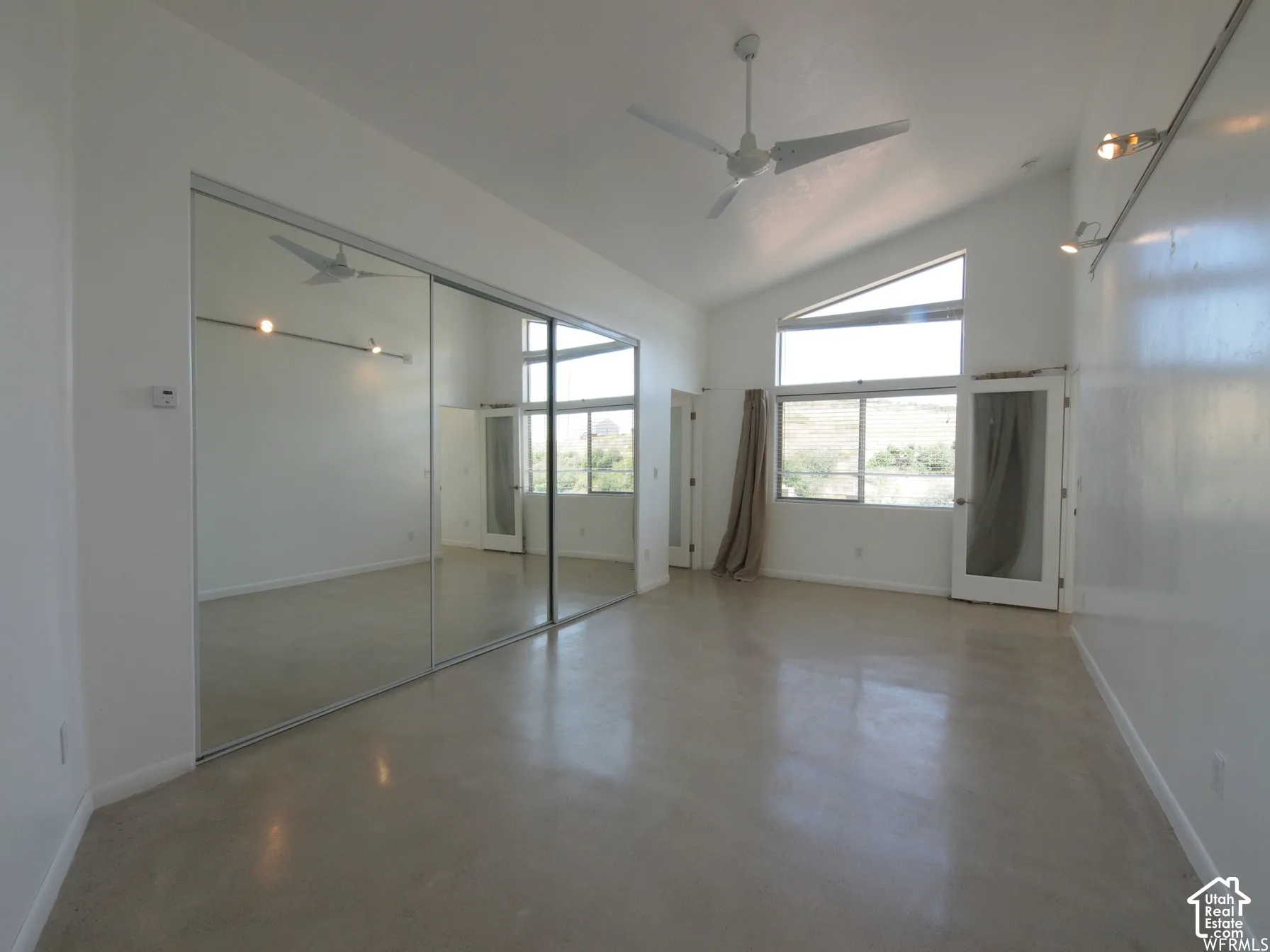 Vaulted ceilings featuring a white ceiling fan, mirrored closet doors, polished concrete flooring, multi-pane windows, and track lighting