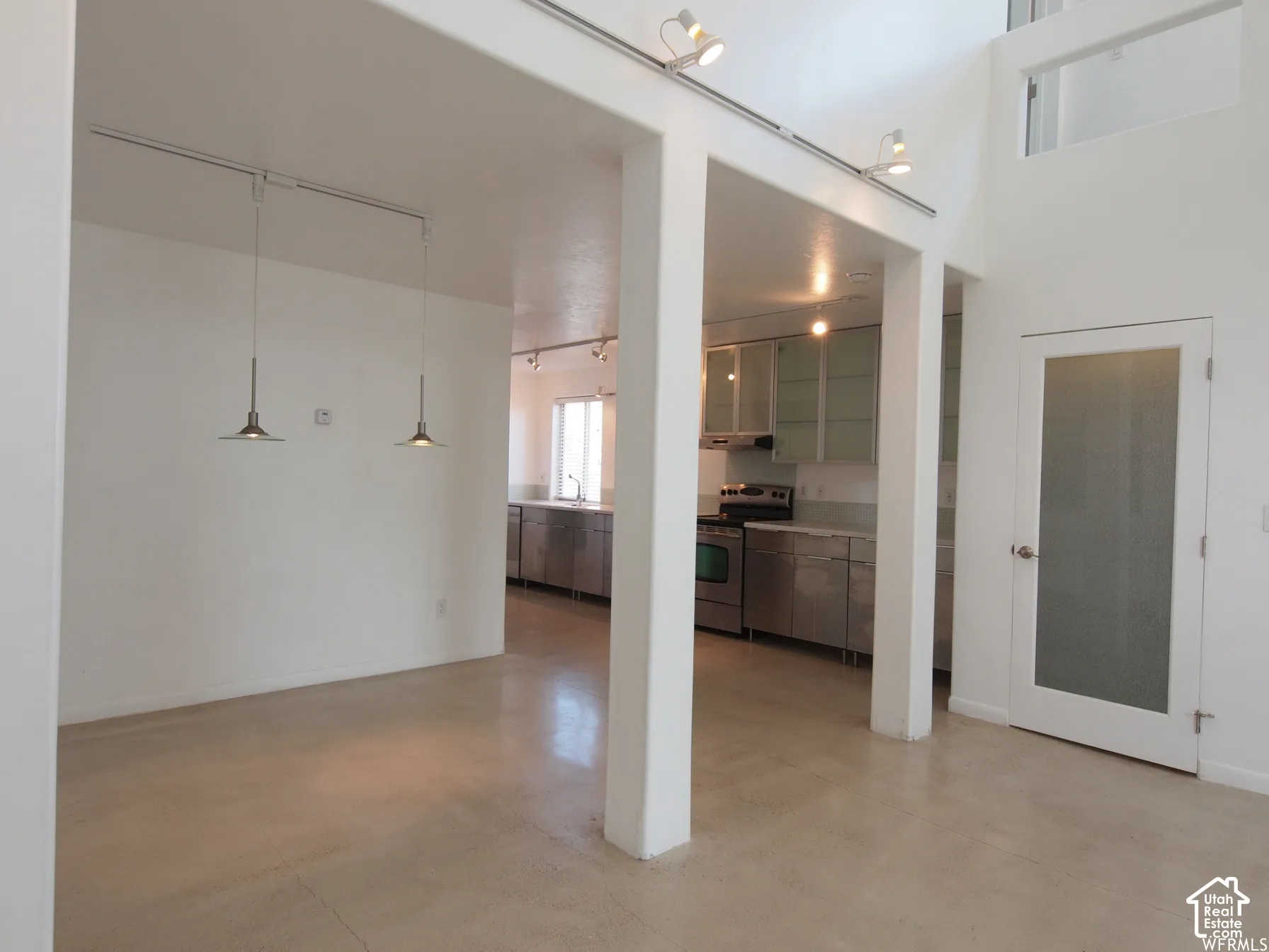 High-ceiling interior featuring polished concrete flooring, industrial track lighting, modern metal cabinetry, and a frosted glass panel door