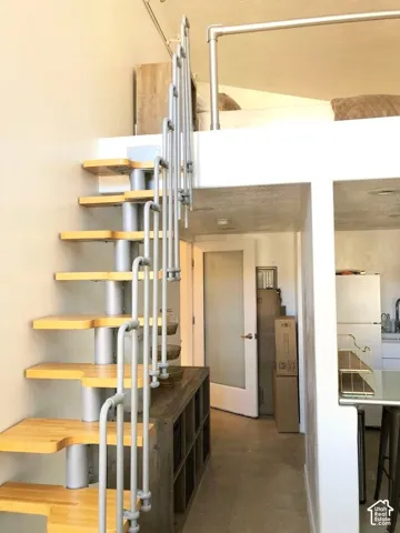 Industrial-style staircase featuring wood-finish treads, a central metal column, and vertical tubular railing leading to an elevated platform with a matching metal guardrail