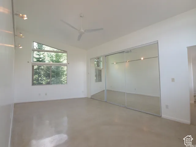 Vaulted ceilings with a ceiling fan, oversized dual-pane windows, polished concrete flooring, and full-wall sliding mirrored closet doors