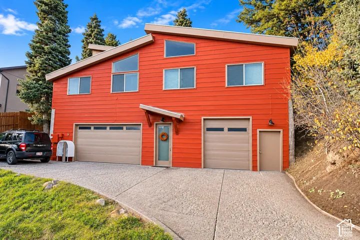 Contemporary residence featuring horizontal wood siding, a shed-style roofline, multi-pane geometric windows, two attached garages, and a concrete driveway