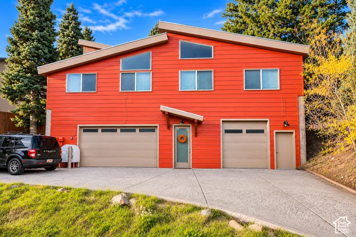 Contemporary two-story exterior featuring vibrant horizontal siding, an asymmetric shed roofline, trapezoidal clerestory windows, and a concrete driveway leading to dual garage bays