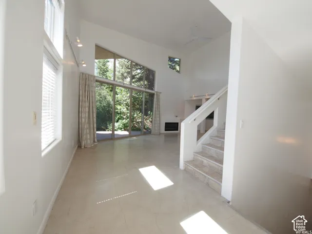 Vaulted ceilings, floor-to-ceiling windows, large-format tile flooring, built-in fireplace, and a white staircase with a prominent railing